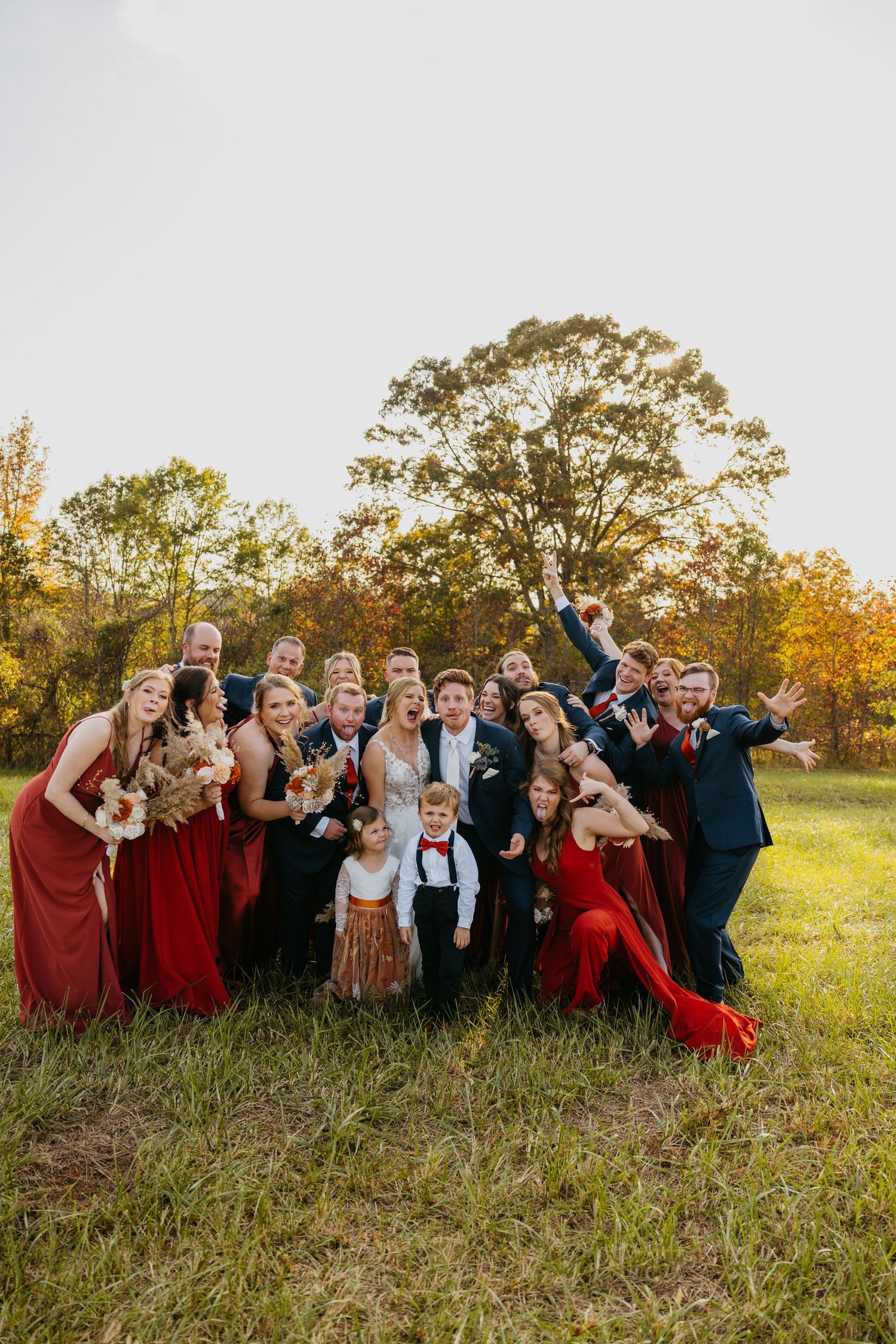 Wedding party in red dresses celebrates joyfully in an autumn field setting.