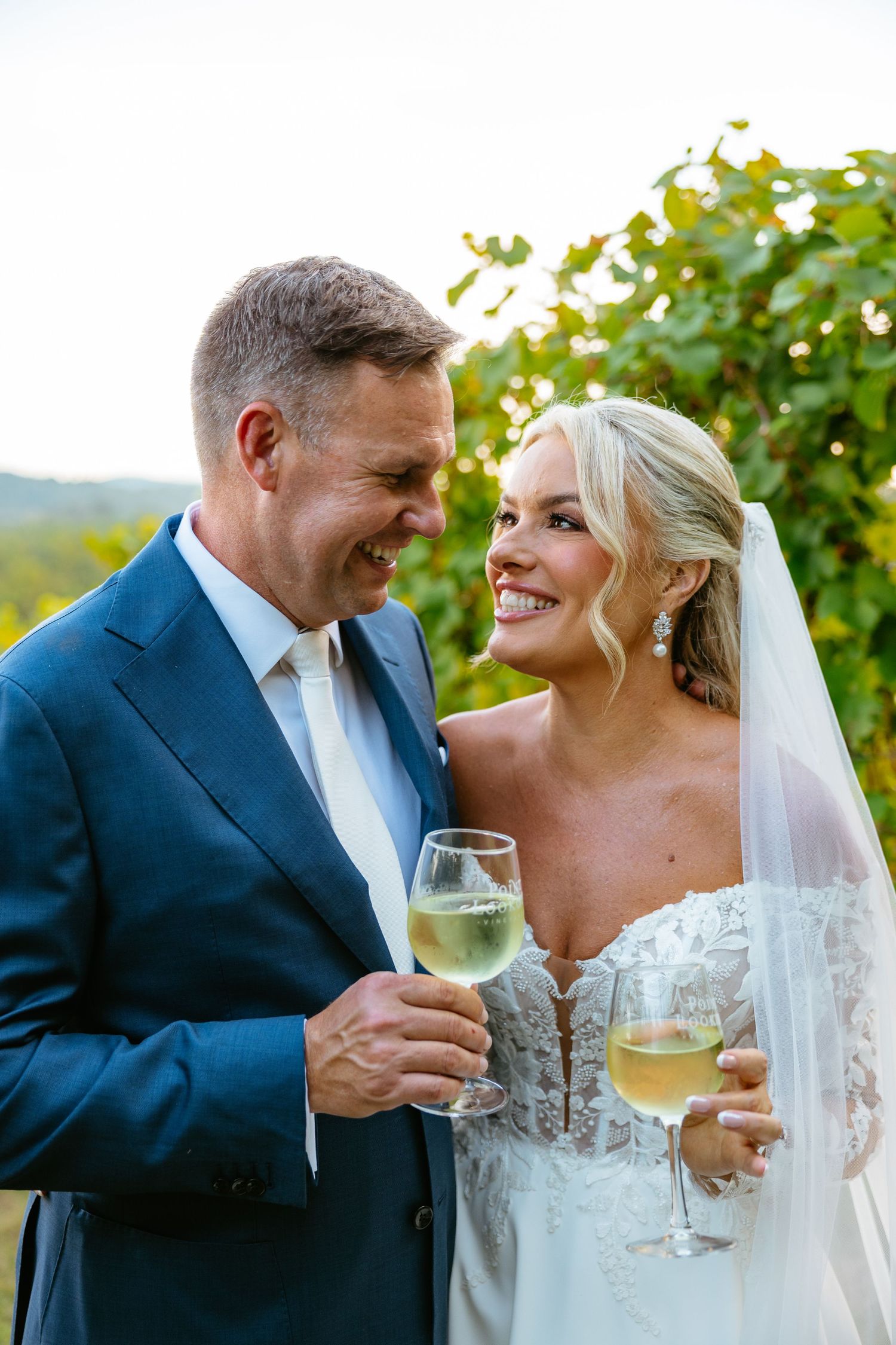 Wedding couple shares intimate moments with champagne glasses amid sunlit vineyard setting.