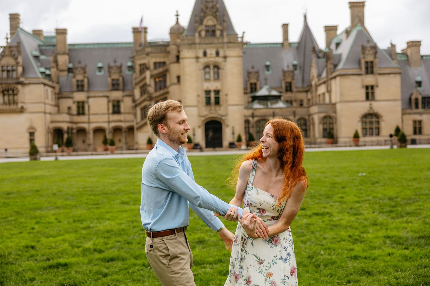 Romantic couple enjoying a sunset dance in a lush green courtyard outside a grand historic mansion.
