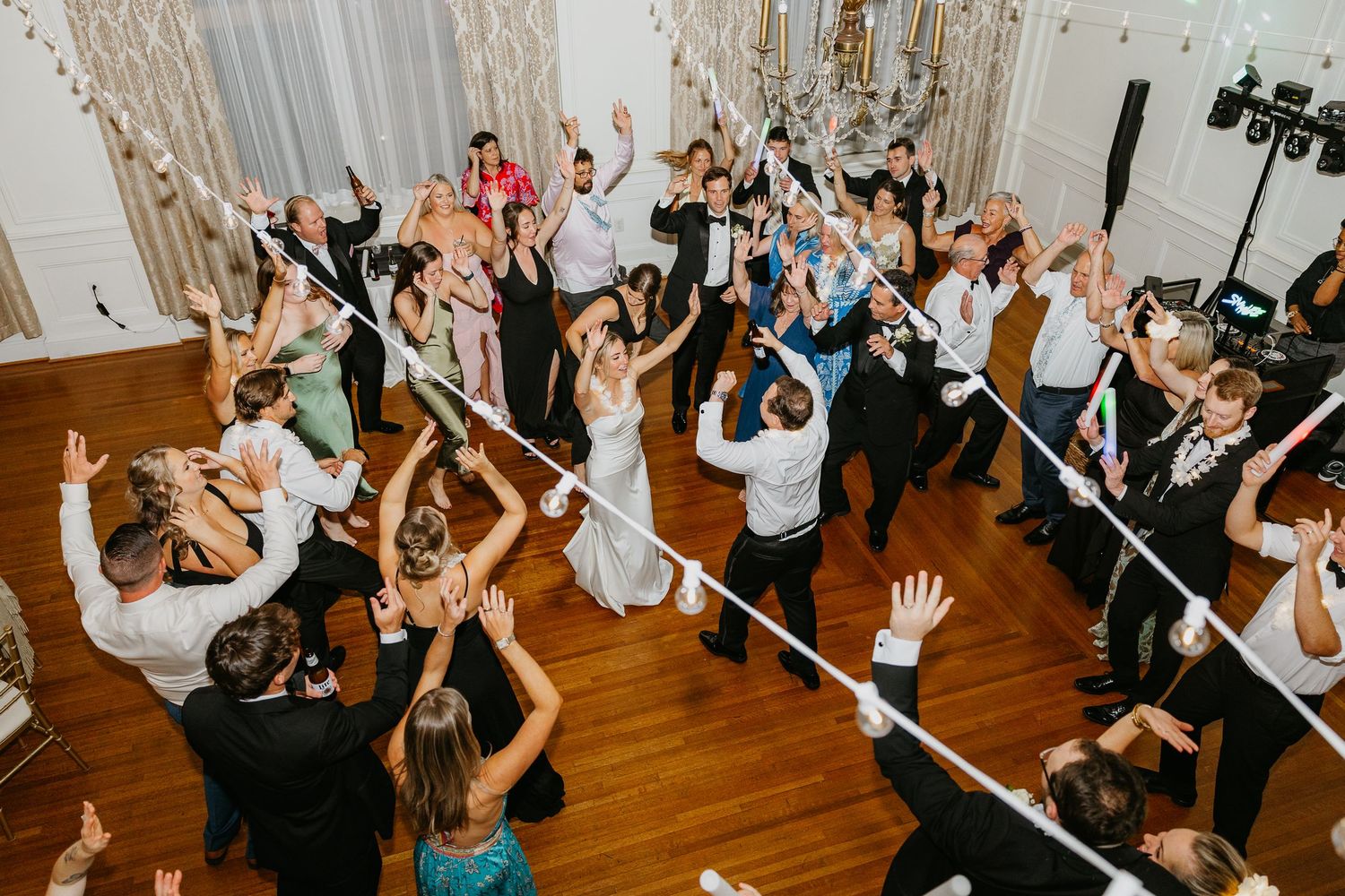 Wedding guests dance and celebrate together on a wooden dance floor during a lively reception party.