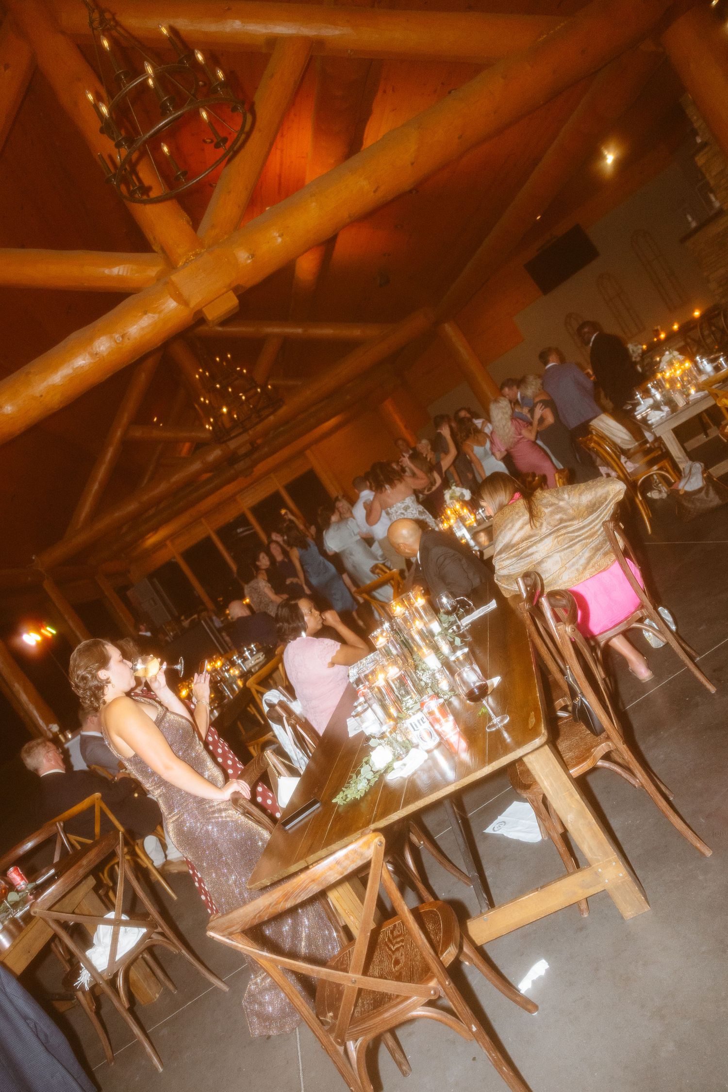 People dancing at a rustic barn reception with wooden beams and twinkling lights overhead creating a warm atmosphere.