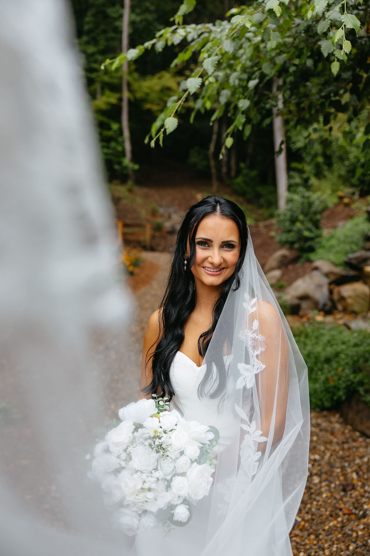Beautiful bridal portrait in a lush forest setting with white floral bouquet and flowing veil.