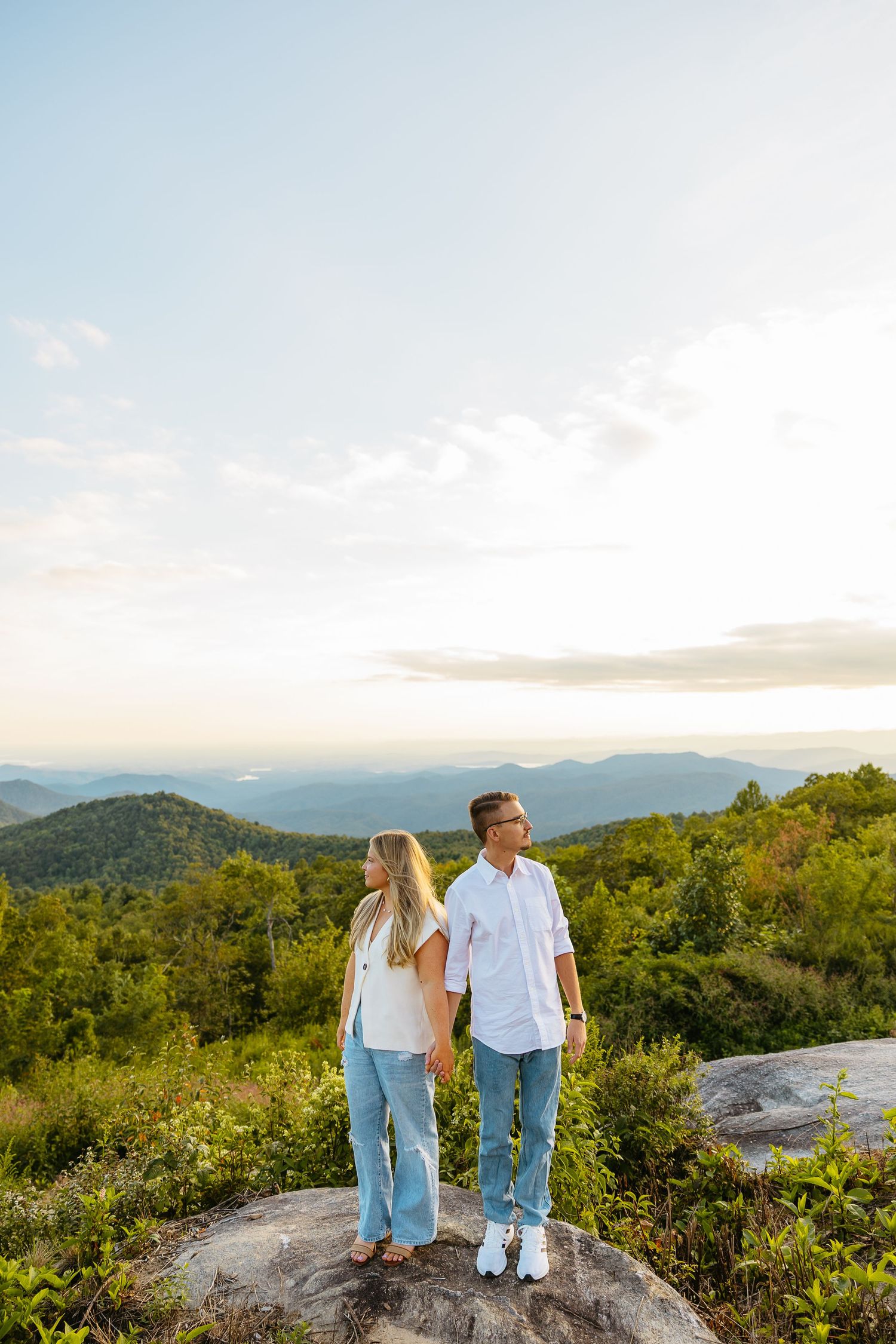 A couple enjoys panoramic mountain views while standing on a rocky overlook during sunset in the Appalachian wilderness.