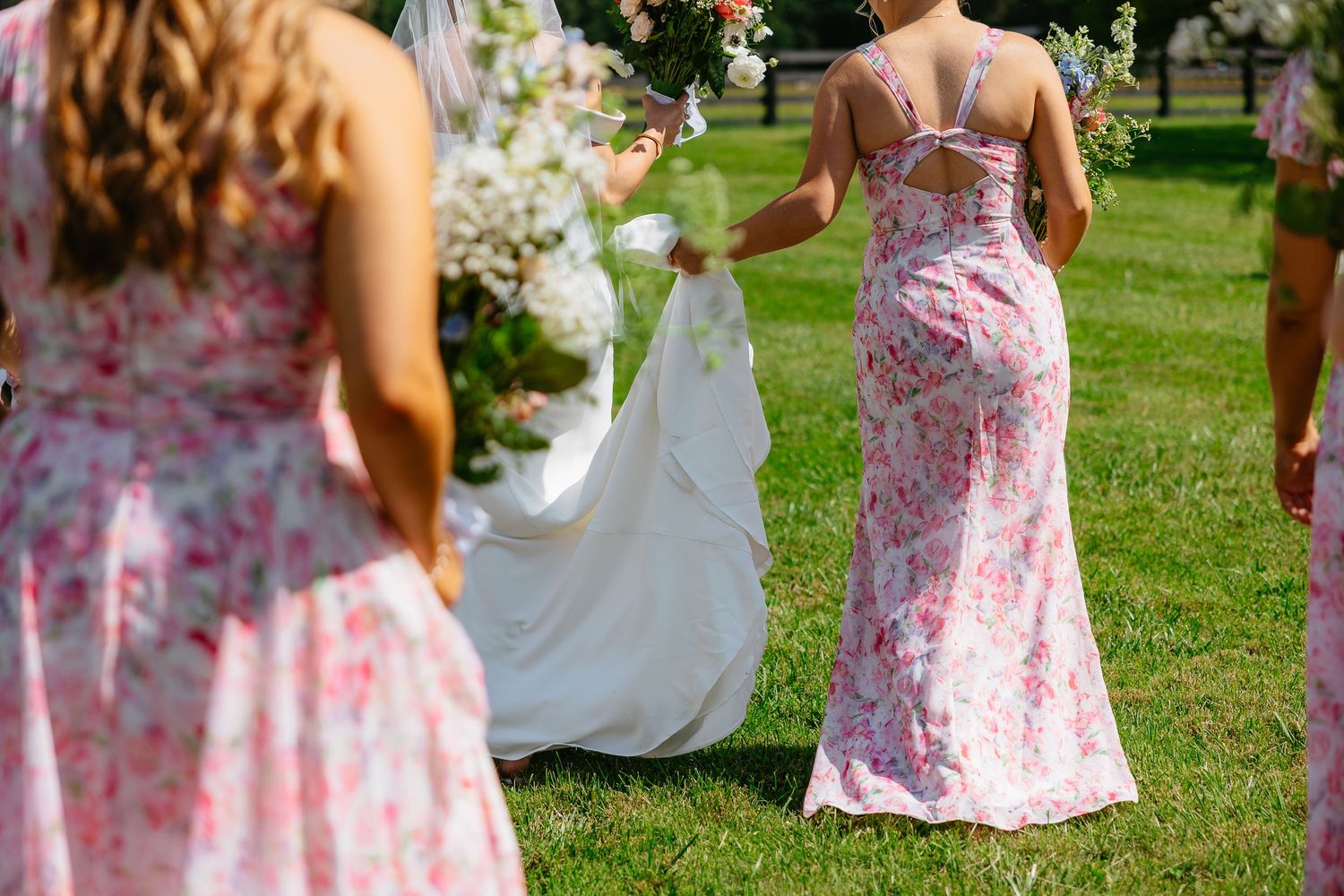 Bridesmaids in floral pink strapless dresses gather on a lush green lawn during an outdoor wedding celebration.