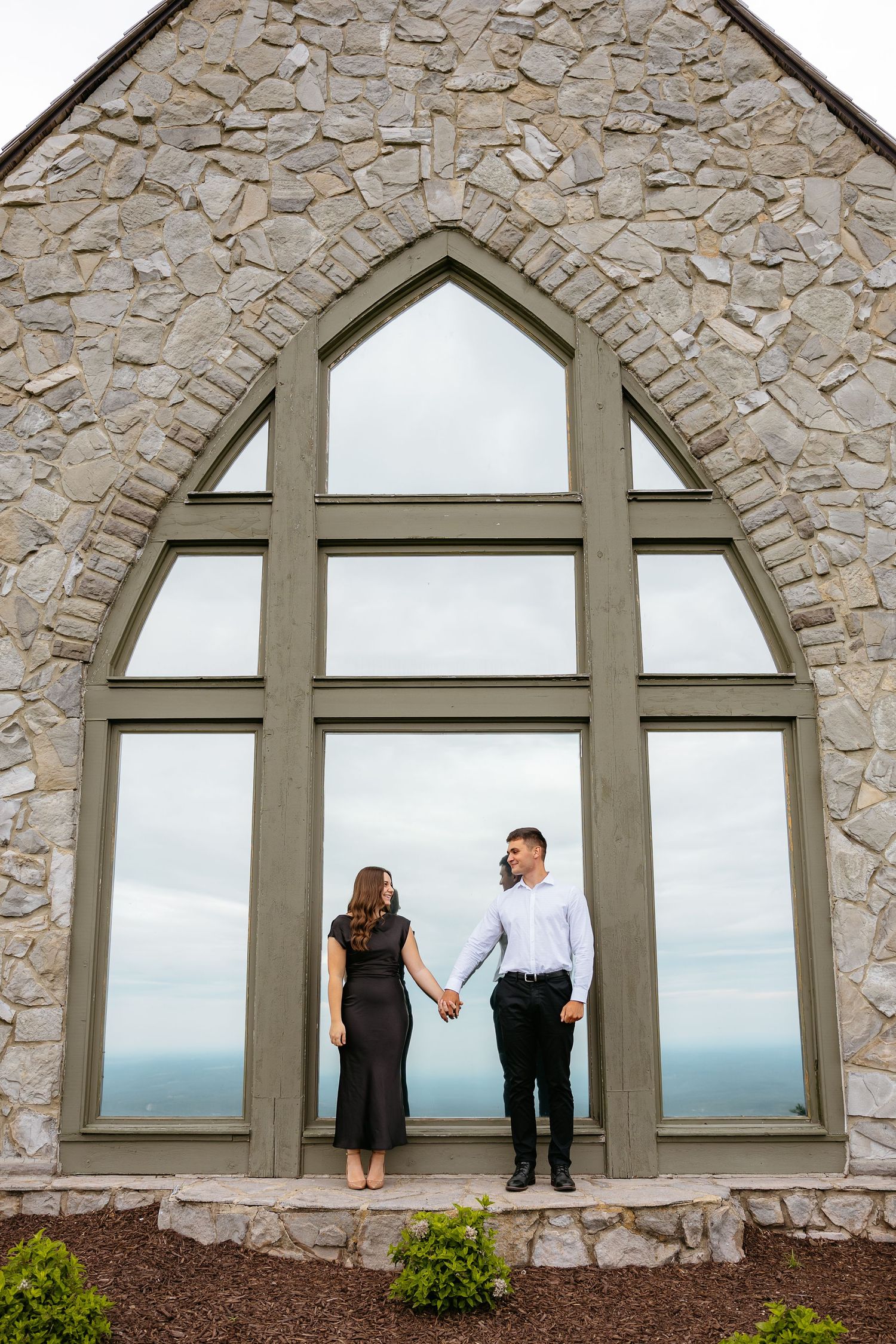 Couple silhouetted against arched stone windows overlooking coastal views in sequence of romantic engagement photos.