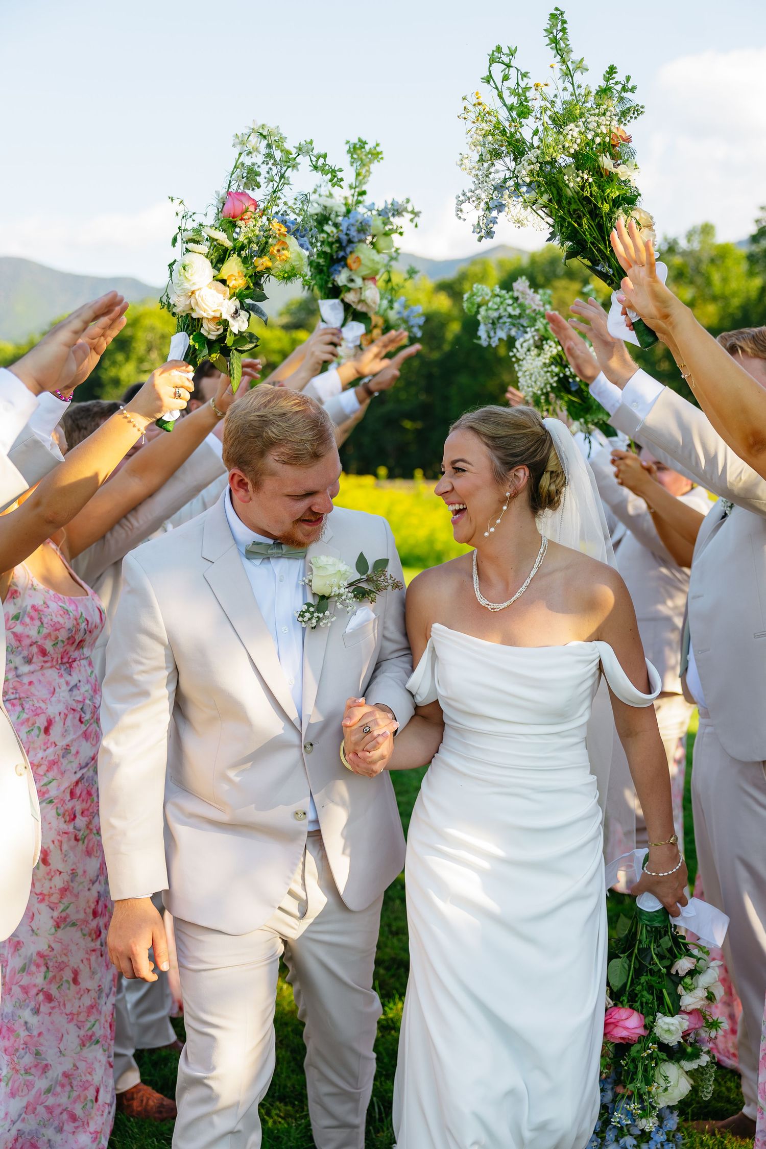 Wedding party celebrates outdoors with raised arms and joyful expressions against natural backdrop.
