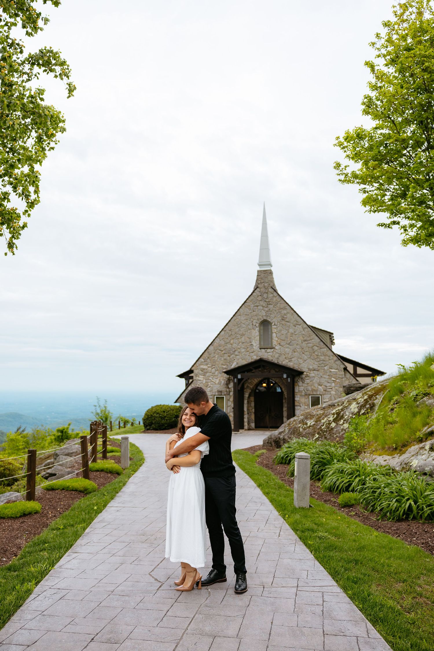 A romantic mountaintop ceremony takes place at a charming stone church with scenic views.