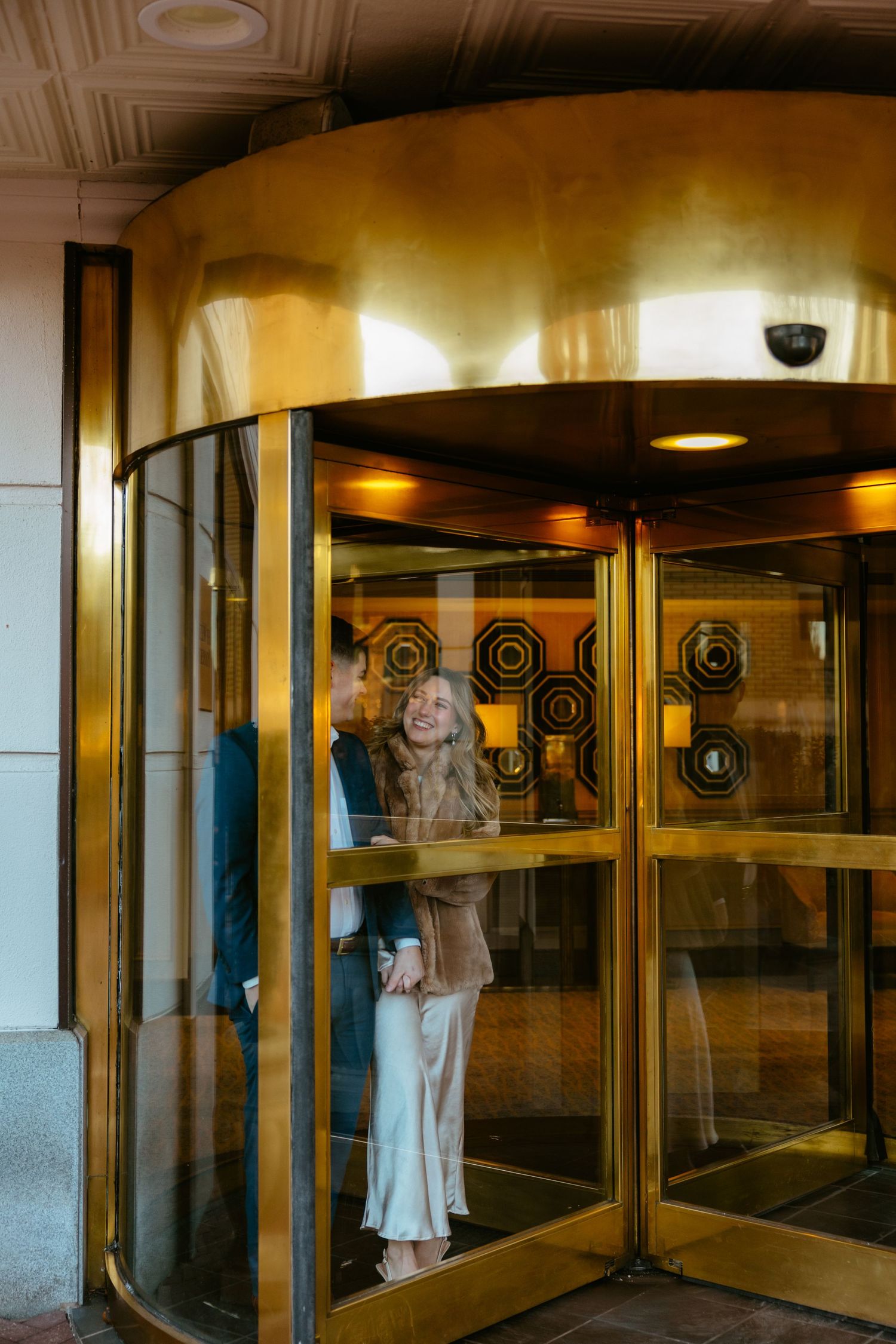 Elegant couple sharing a moment in a golden revolving door of a luxury building.