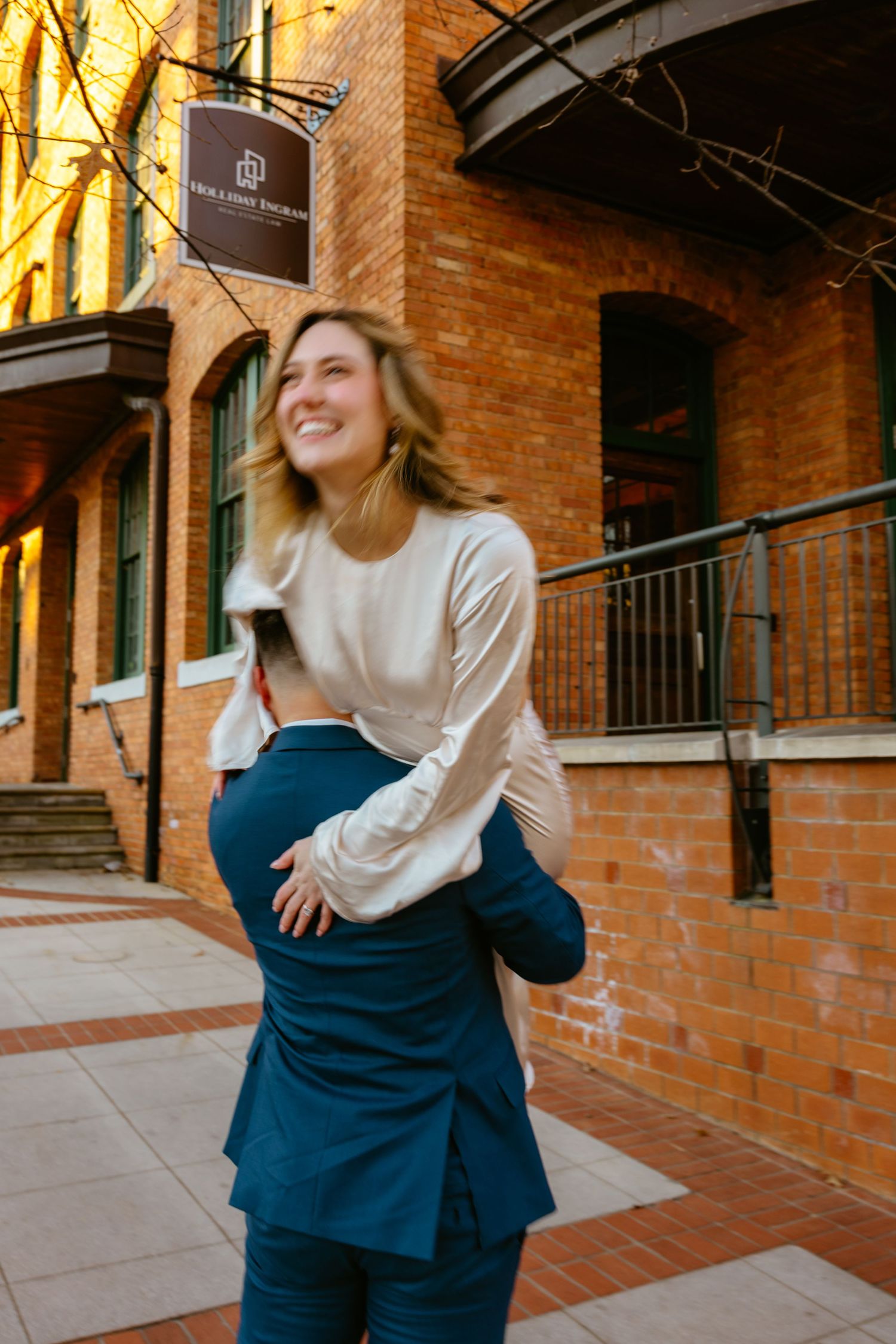 Joyful woman in casual attire laughing outside a brick building during golden hour.