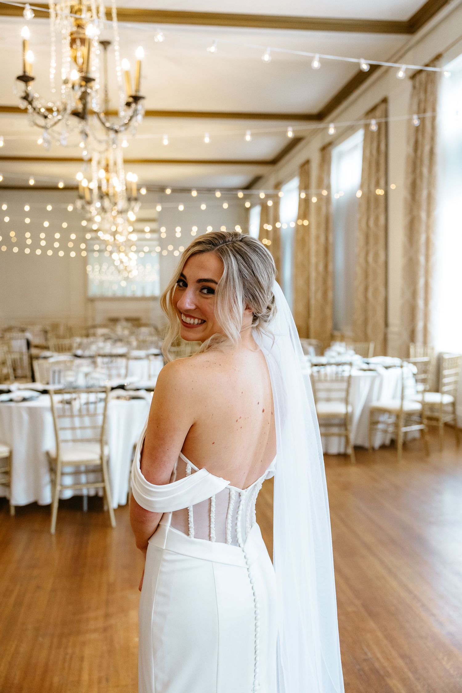 Bridal photos in an elegant ballroom with hardwood floors, crystal chandeliers and white wedding chairs.