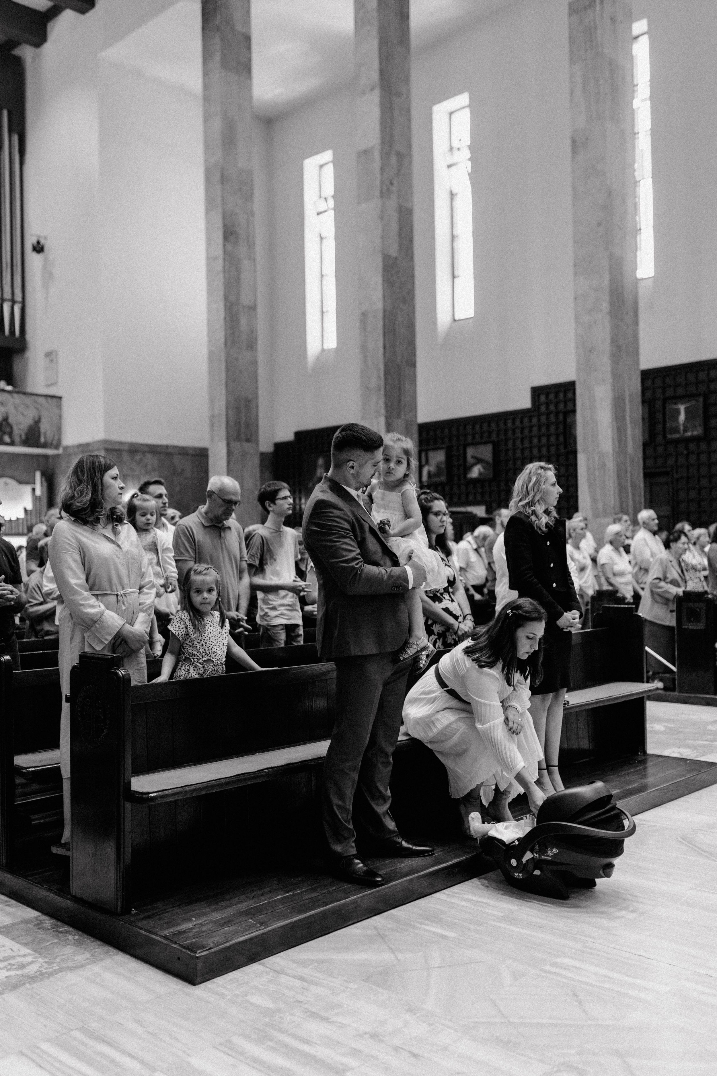 Wide shot of the congregation, with the family in focus sitting in the front row during the christening ceremony.