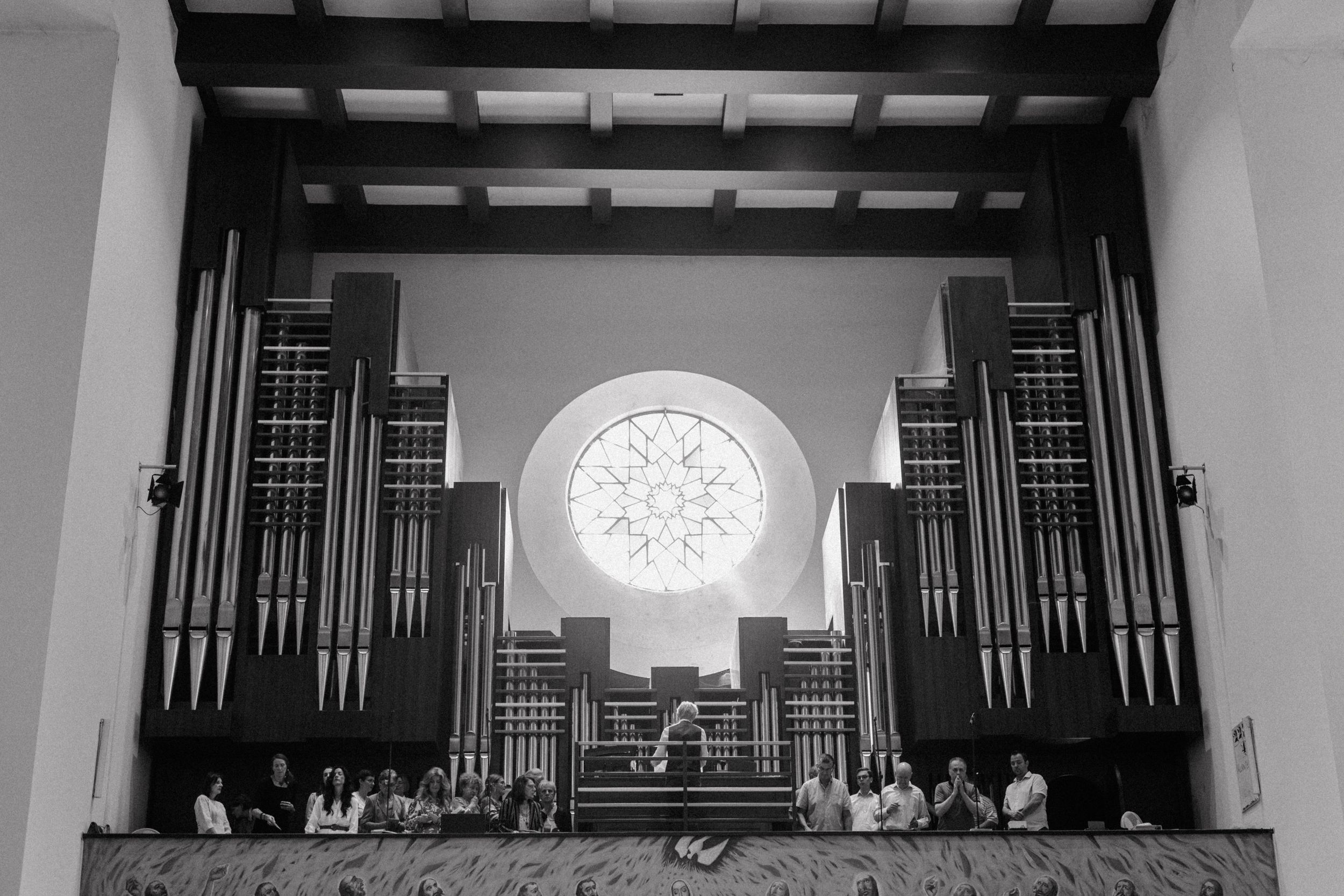 Interior of a grand church showing pipe organ and round stained glass window in black and white.