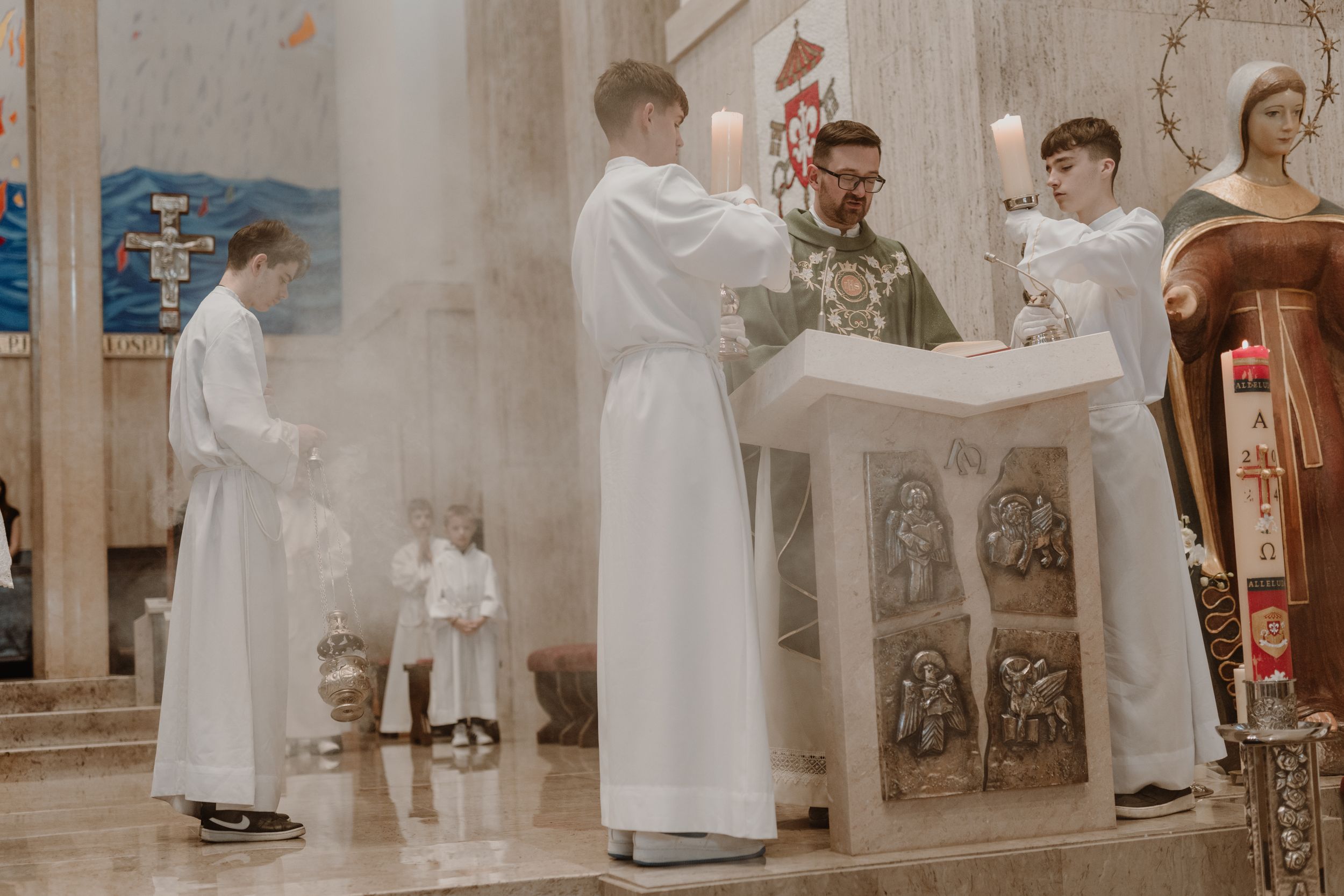 Wide shot of the priest praying while altar boys hold candles during the christening ceremony.