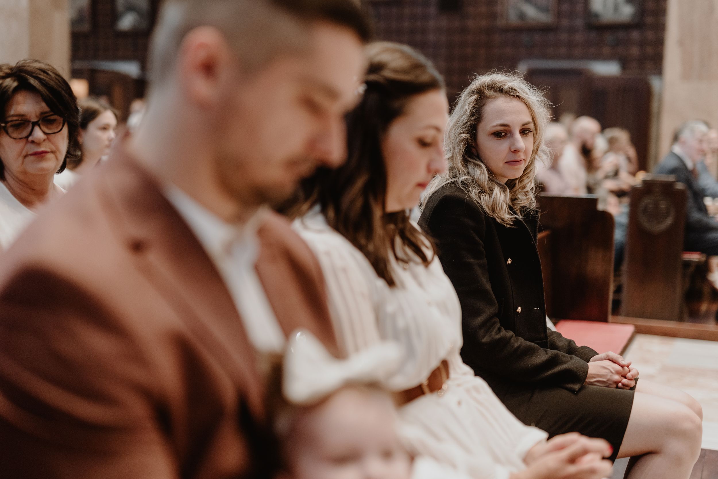 Godmother gazing lovingly at the child while the father is softly out of focus in the foreground during the christening.