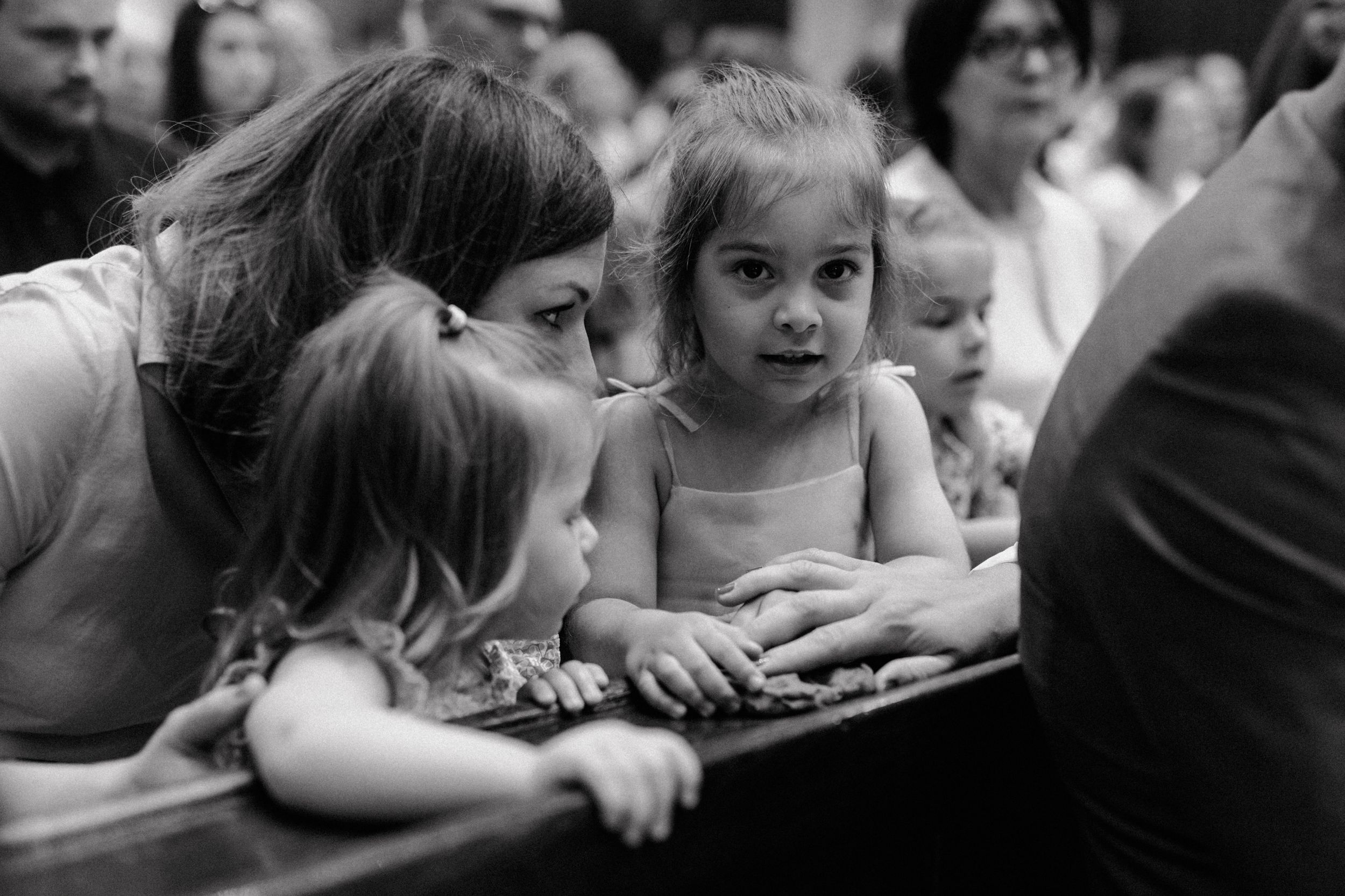 Black and white photo of children sitting in the second row, attentively observing the christening ceremony.