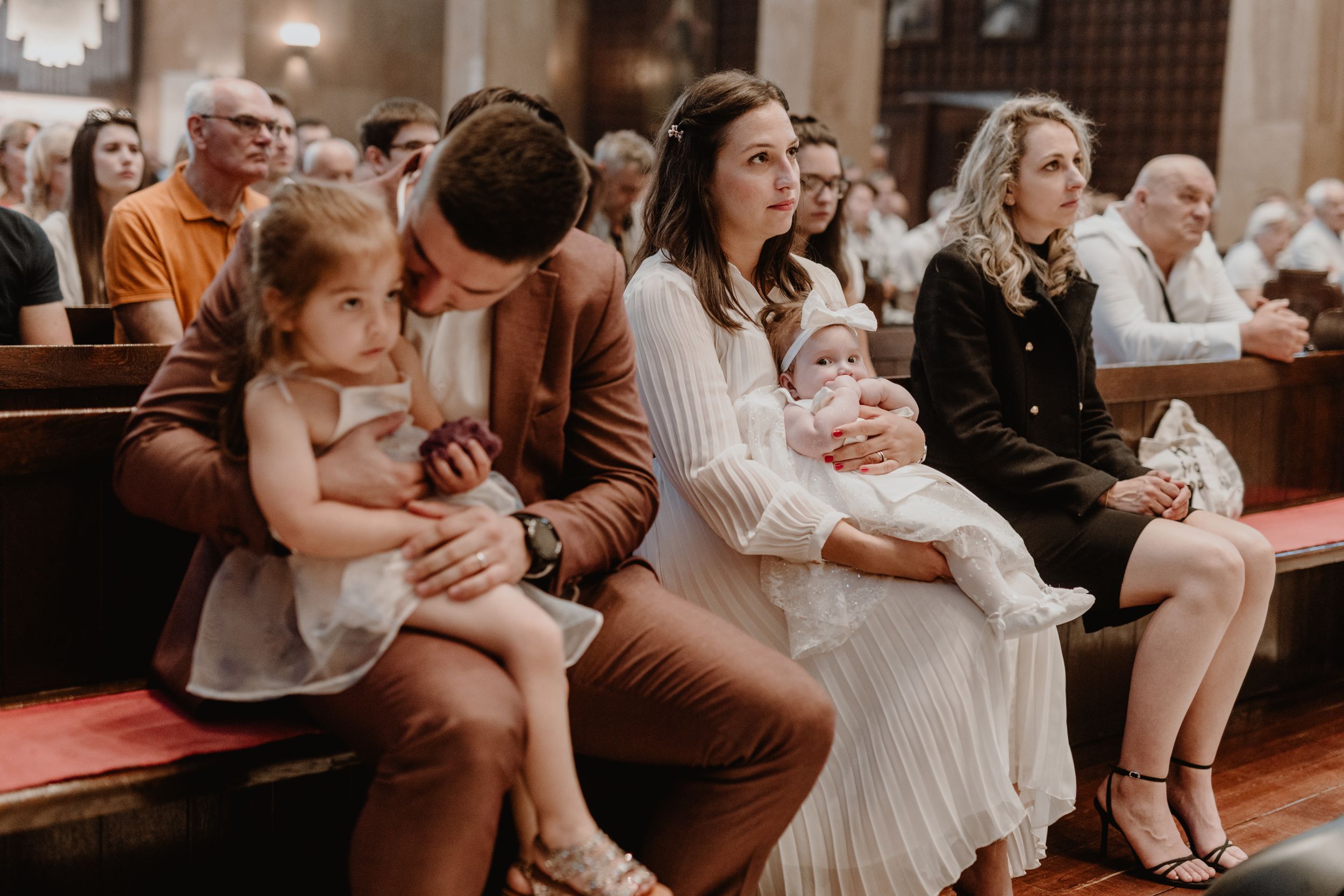 Dad kisses his daughter while holding her on his lap, with mom clearly in focus and the front row of the church.