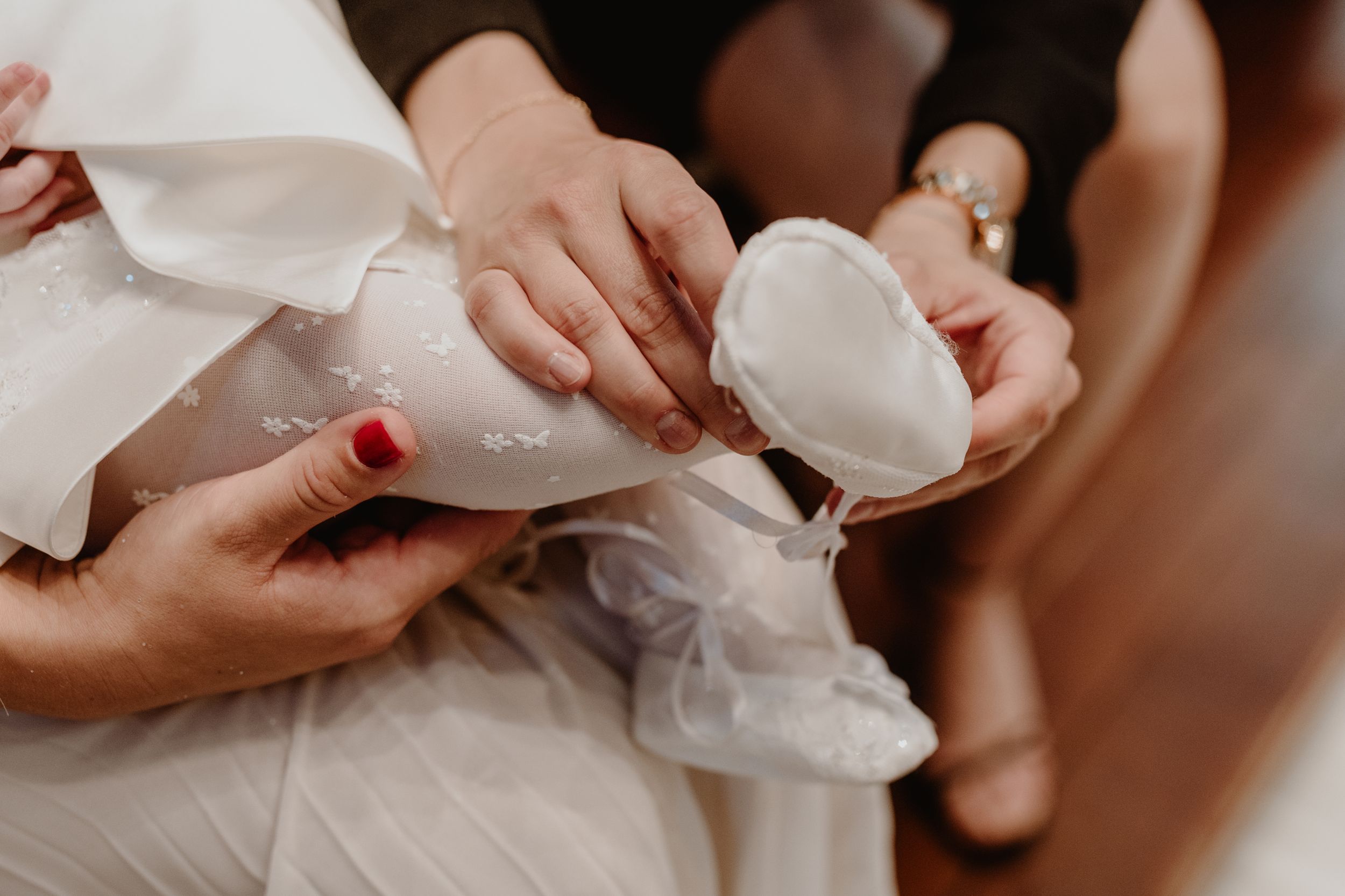 Close-up detail of a tiny shoe being gently placed on the baby’s foot during the christening ceremony.