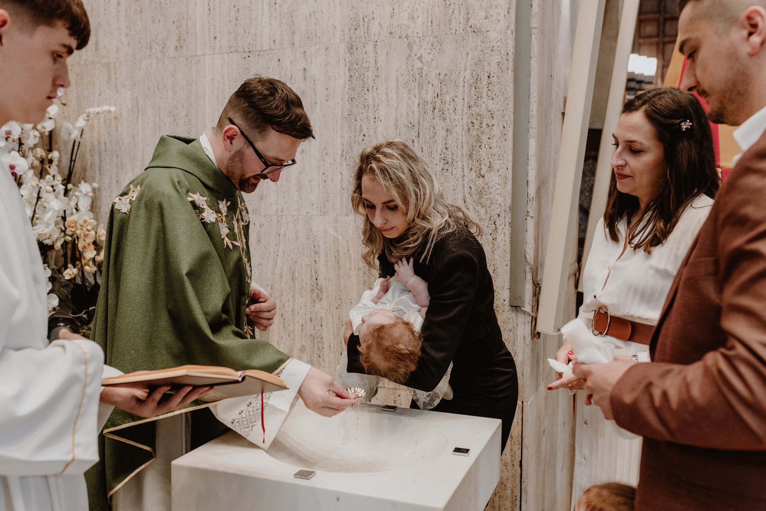 Family gathered with the priest at the baptismal font, godmother holding the baby moments before the christenining.