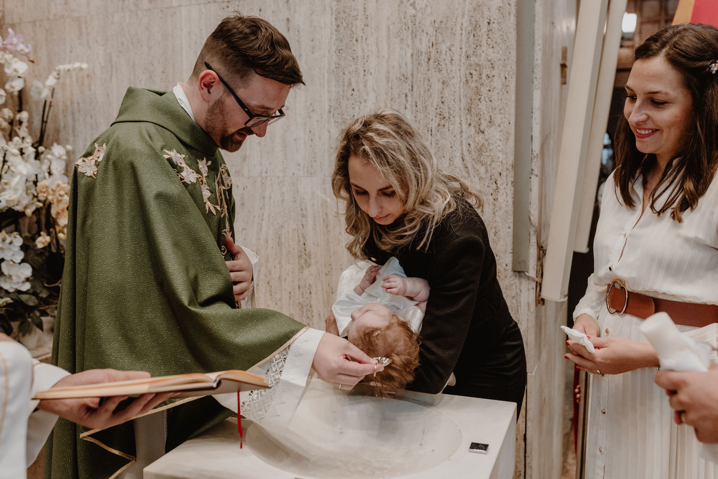 Family gathered around the baptismal font as the priest pours holy water on the baby during the christening ceremony.