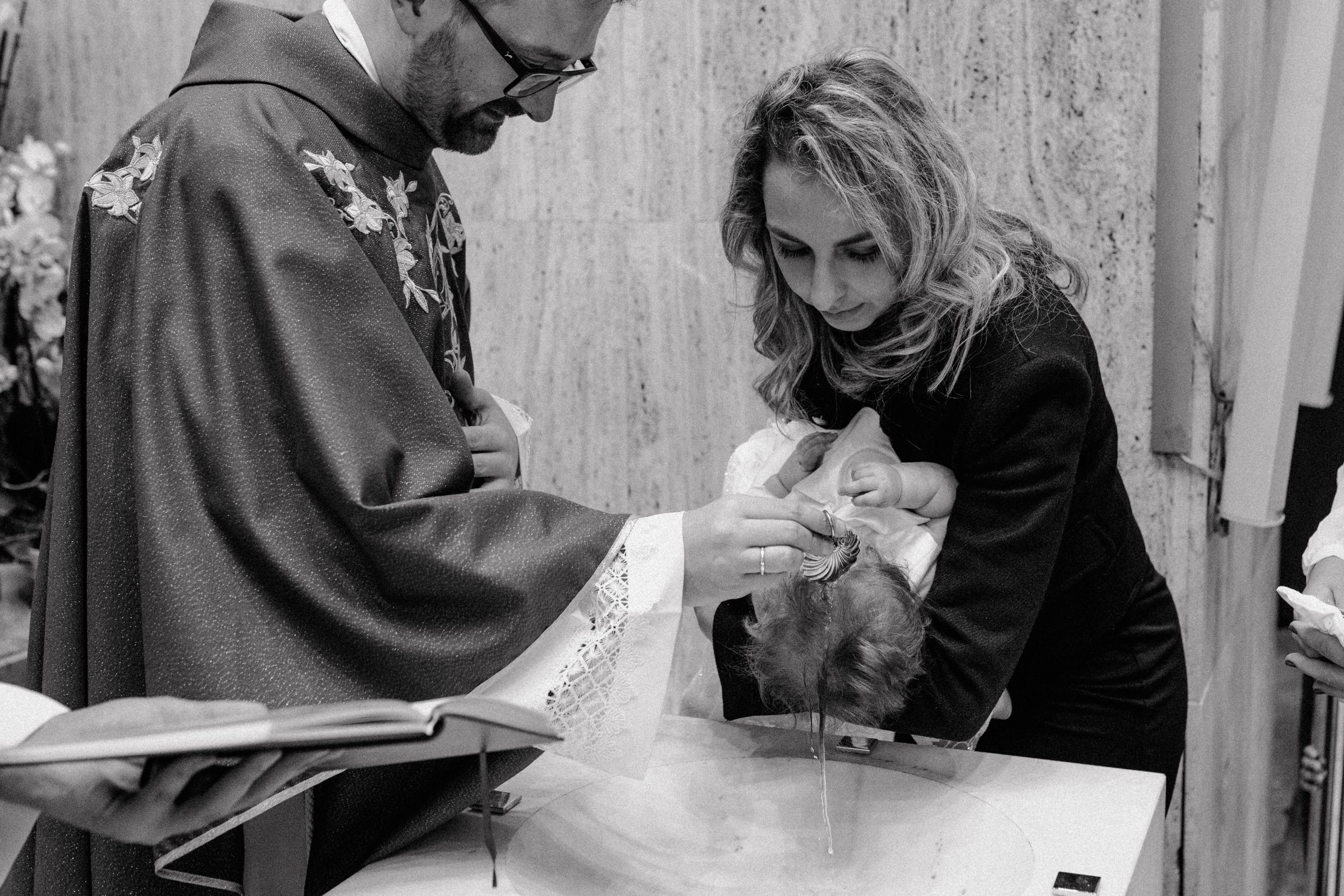 Black and white close-up of a priest gently pouring water over the baby's head during the christening ceremony in Zagreb