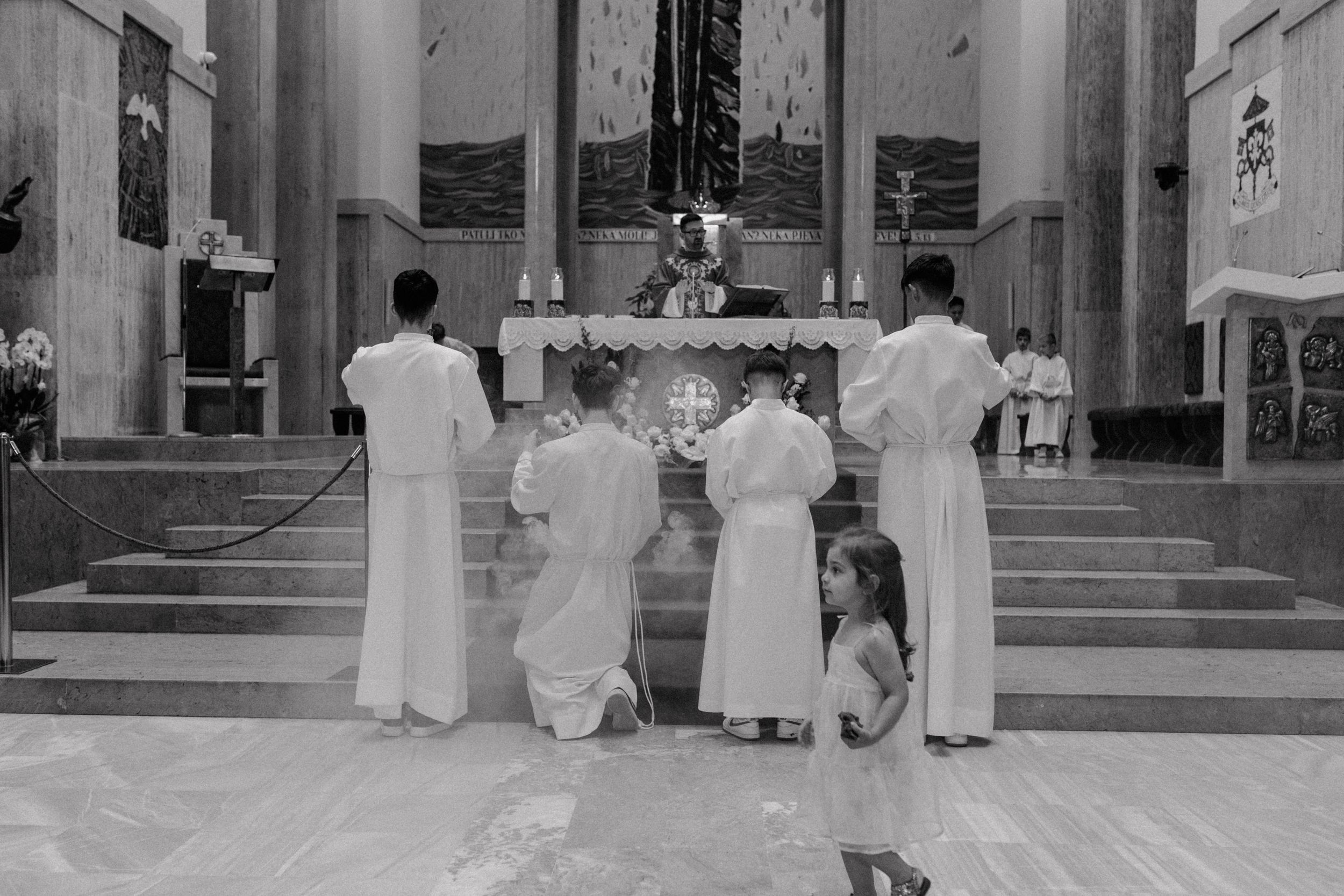 Altar boys kneeling in front of the altar, the daughter passing by out of focus in the foreground during christening.