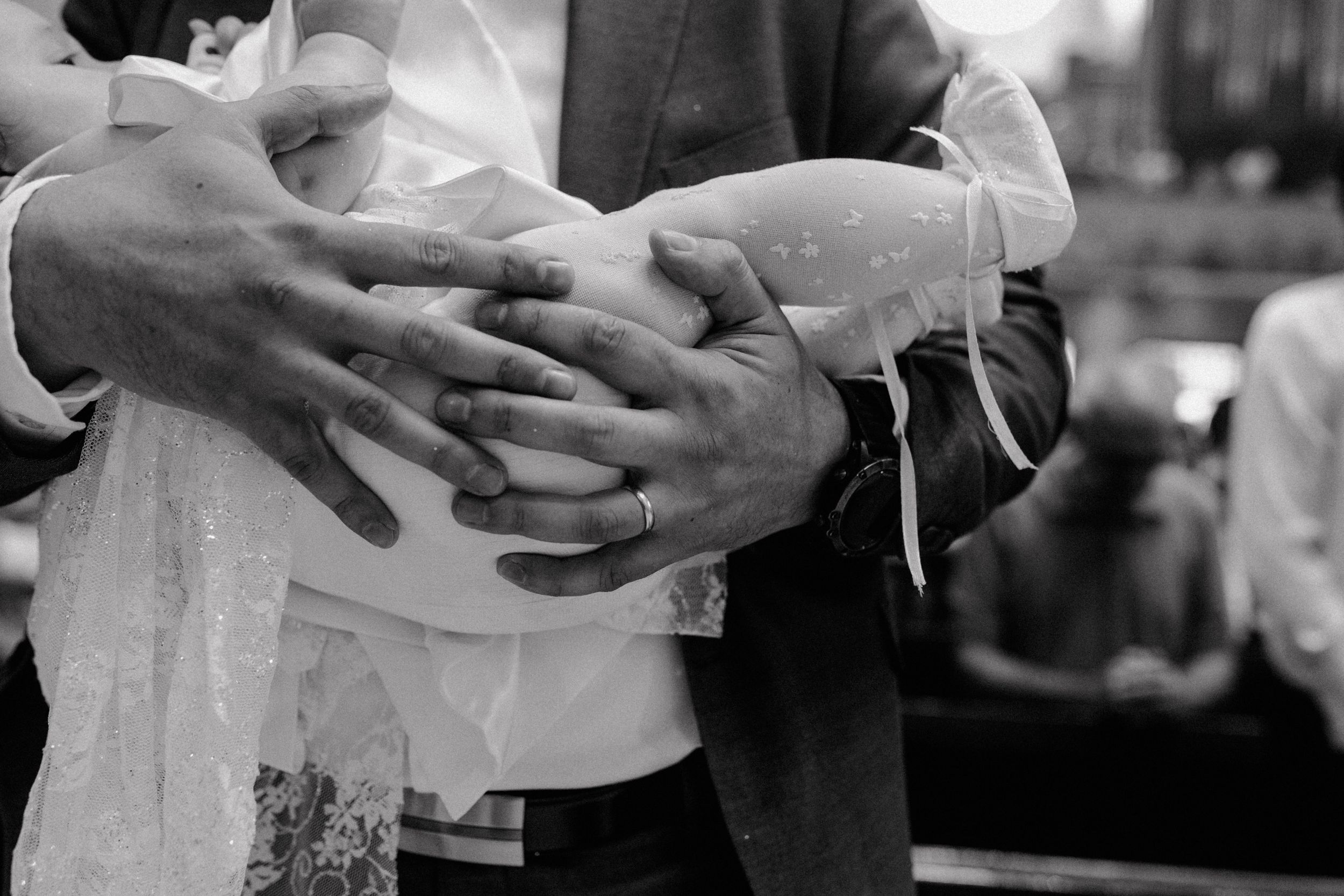Black and white close-up of the dad's hands gently holding the baby, highlighting the loving and protective touch.