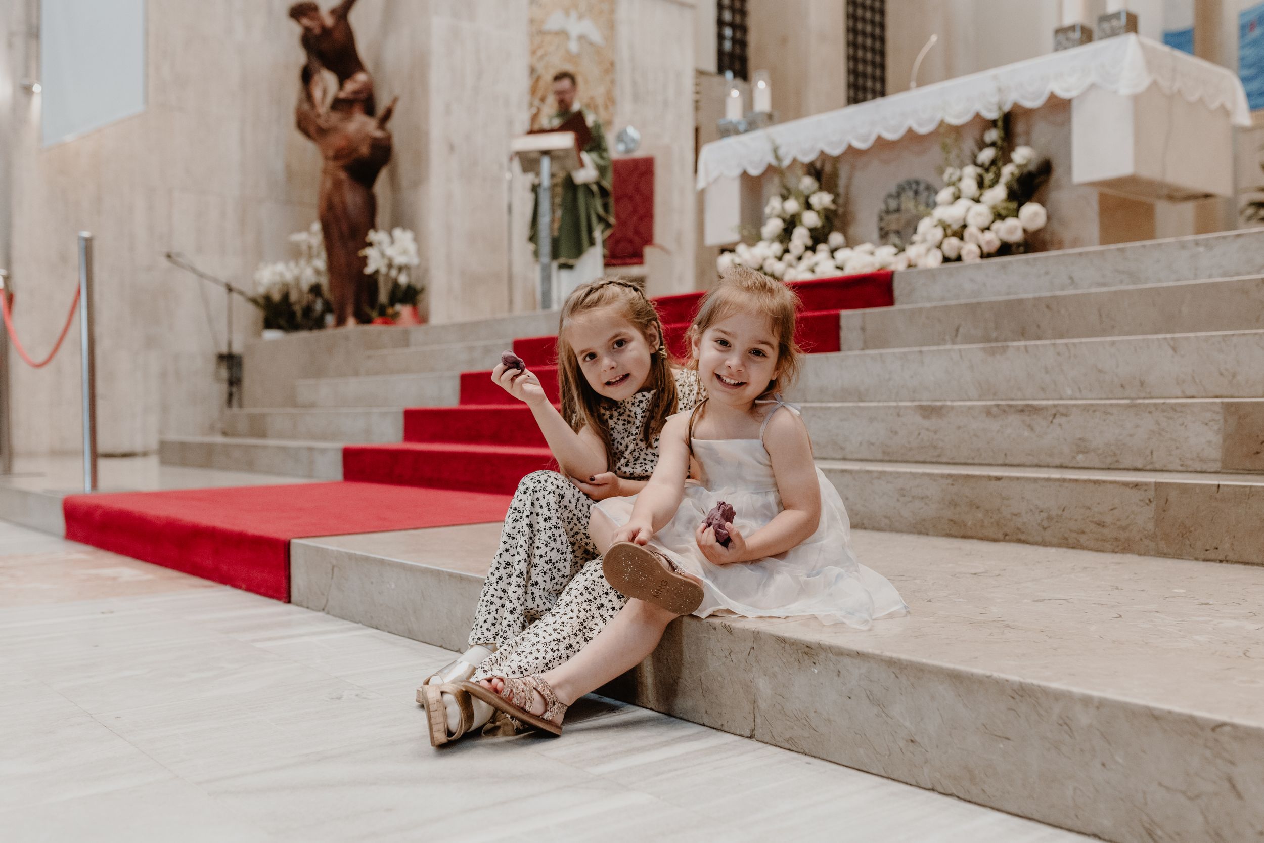 Portrait of an older daughter and her friend sitting quietly next to the altar during the christening ceremony.
