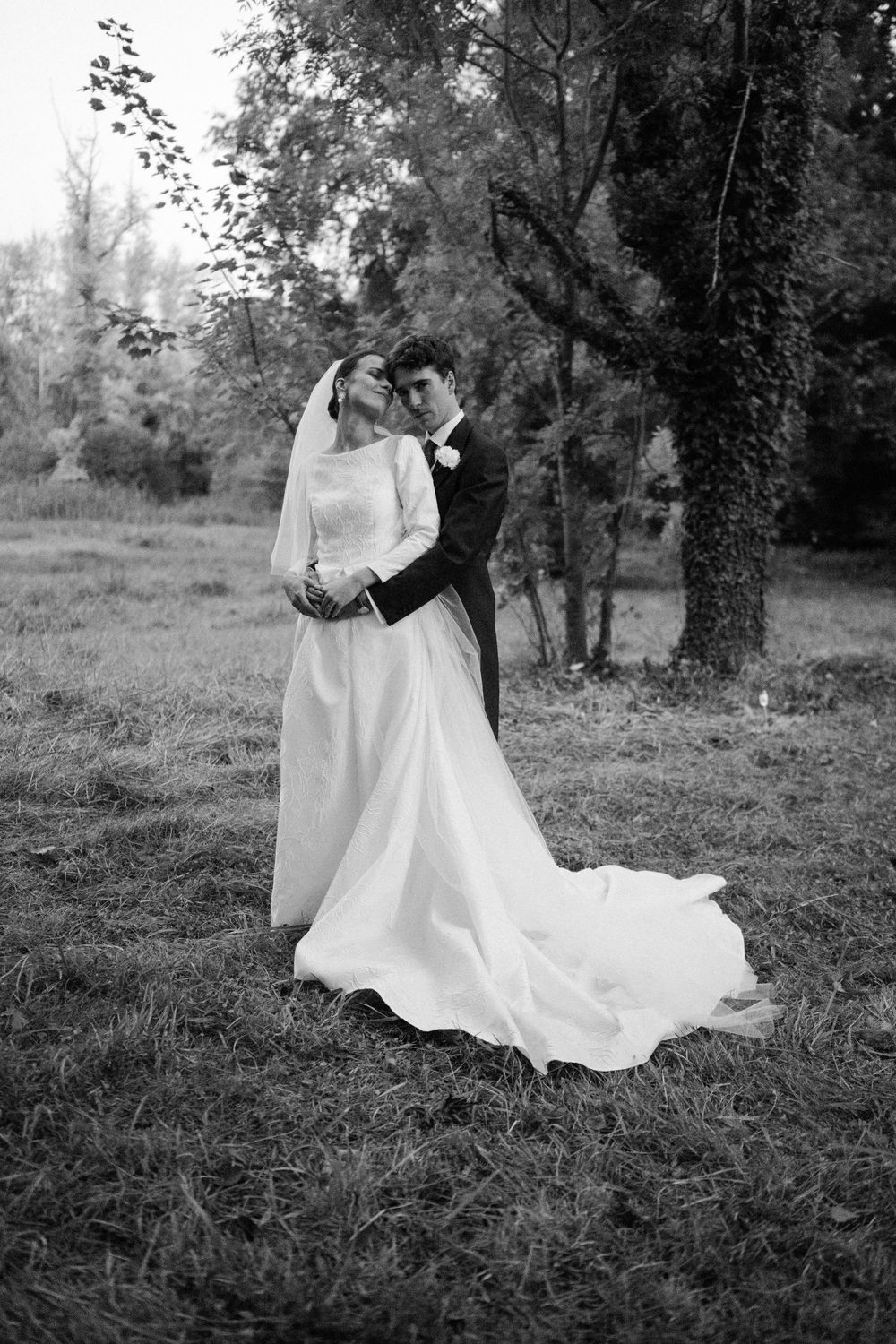 A romantic black and white wedding photo showing a couple embracing outdoors with a flowing white dress and natural backdrop.