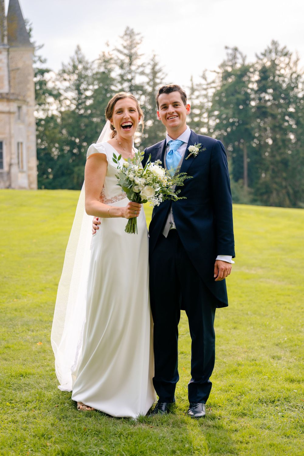 A couple shares joyful moments on their wedding day while standing together on a lush green lawn.