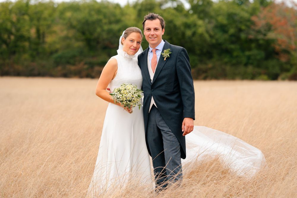 A couple in wedding attire walks together through a golden wheat field during sunset.