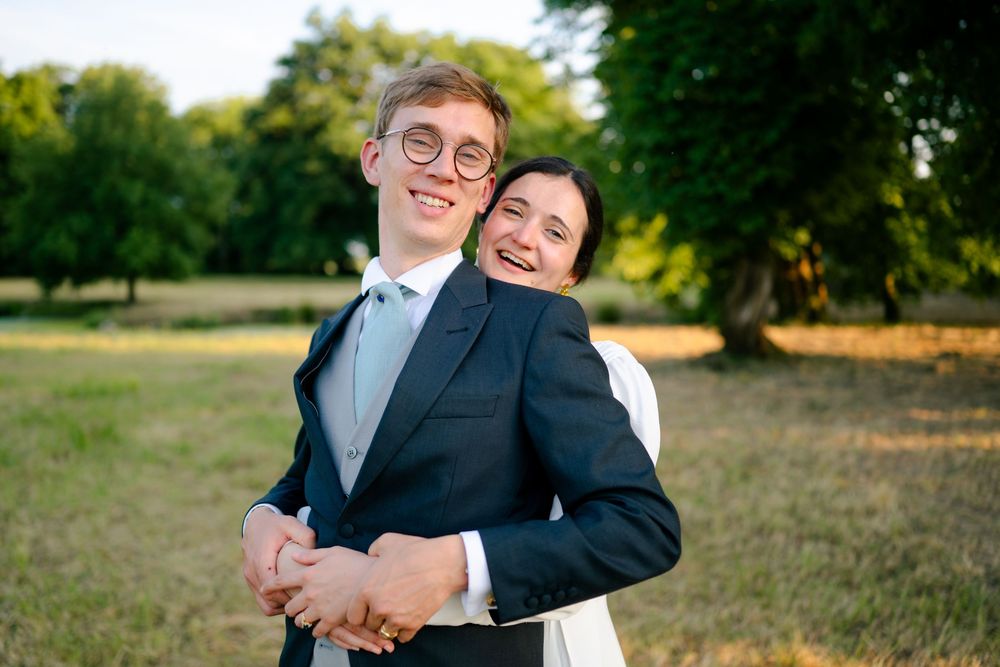 A happy couple embraces while posing outdoors in formal attire during a sunset photo session in a park.