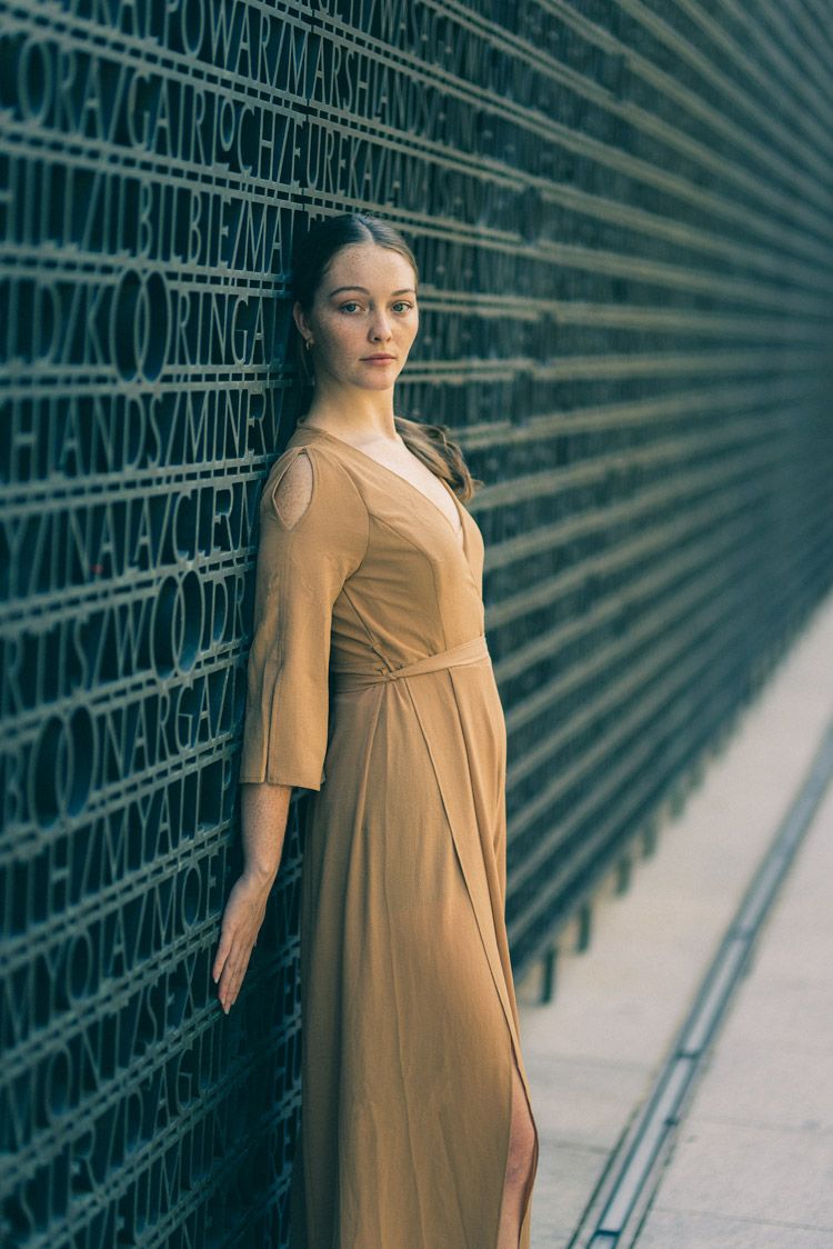 Elegant woman in flowing dress poses against wall. Headshots photography by Nick Wigmore Photography.