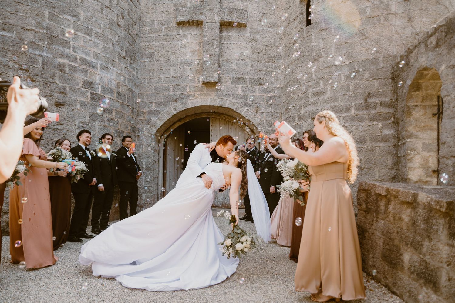 Bride & Groom kiss as they exit Otttis Castle in St. Augustine, with bubbles and people cheering. Cred: LexTakePix