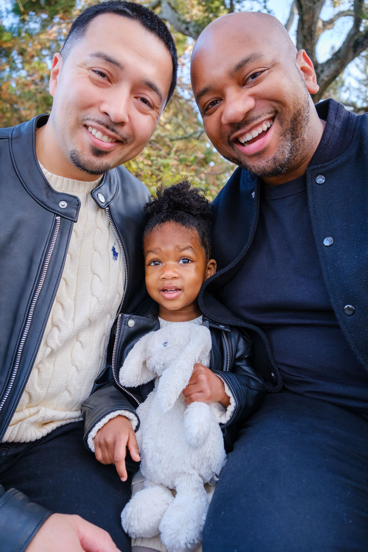 A joyful family shares genuine laughter together while sitting on an outdoor porch during a casual photo session.