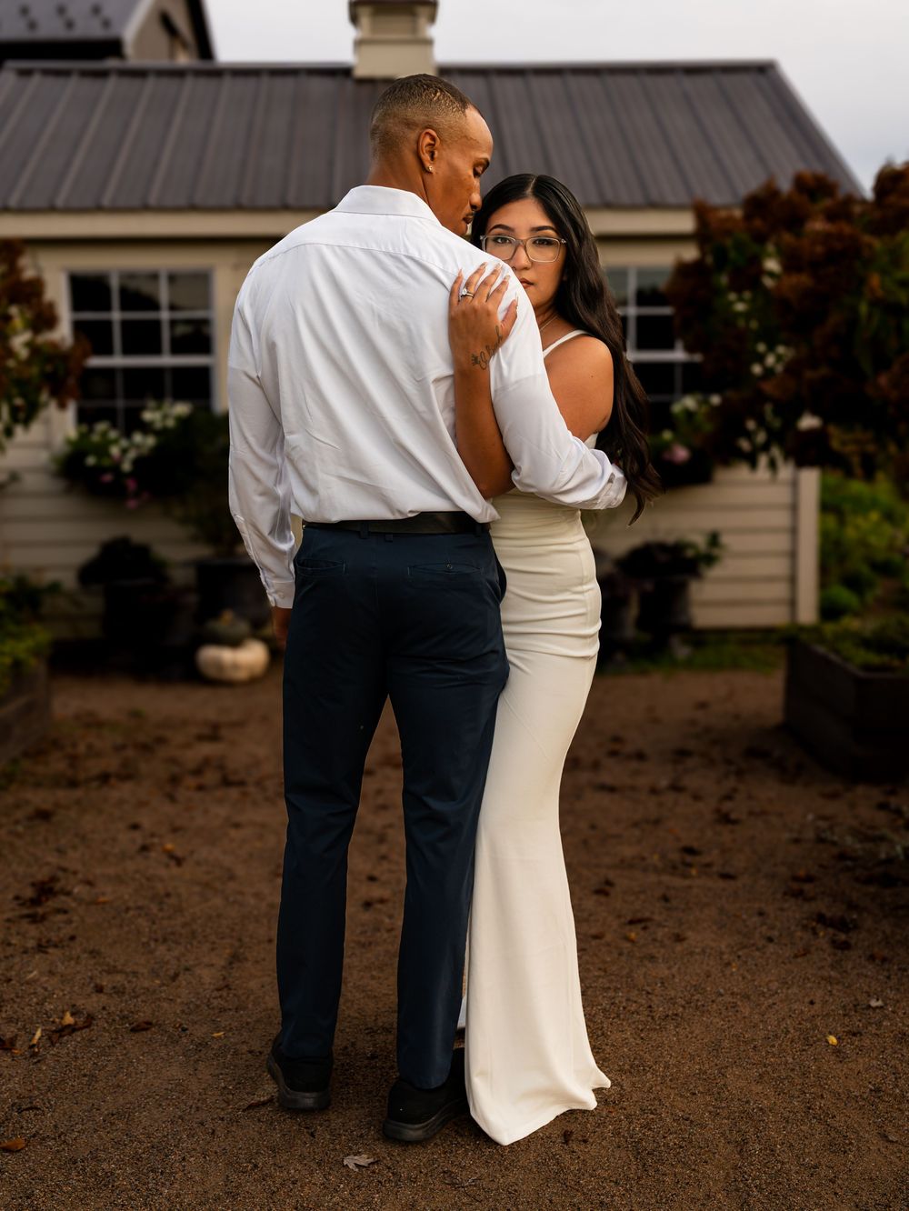 A couple in formal attire embraces during a romantic outdoor photoshoot against a building backdrop.