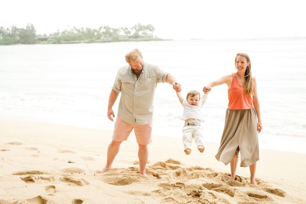 Parents playing with child on sandy beach at sunset. Oahu Family Photographer