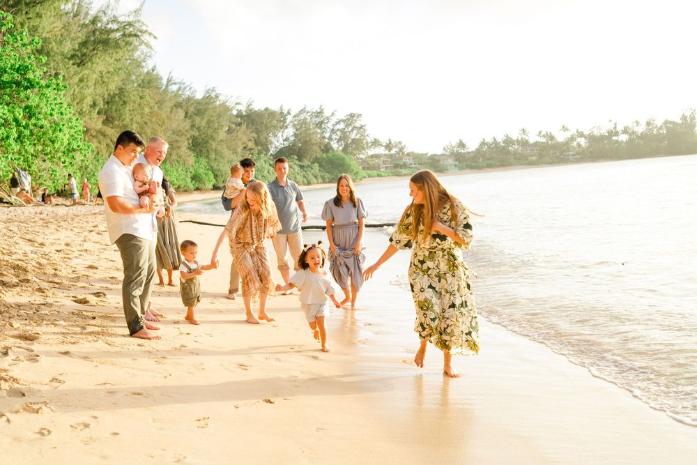 Group walking along a scenic beach shoreline at sunset in tropical attire. Oahu Family Photographer