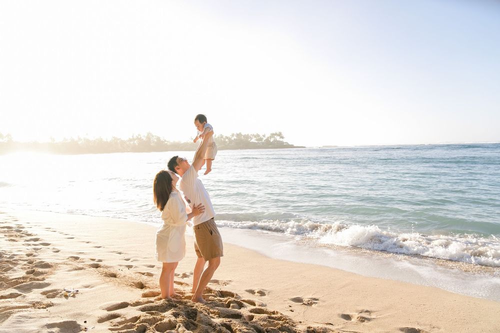 A couple walks along a sandy beach at sunset with ocean waves rolling onto the shore in the background.