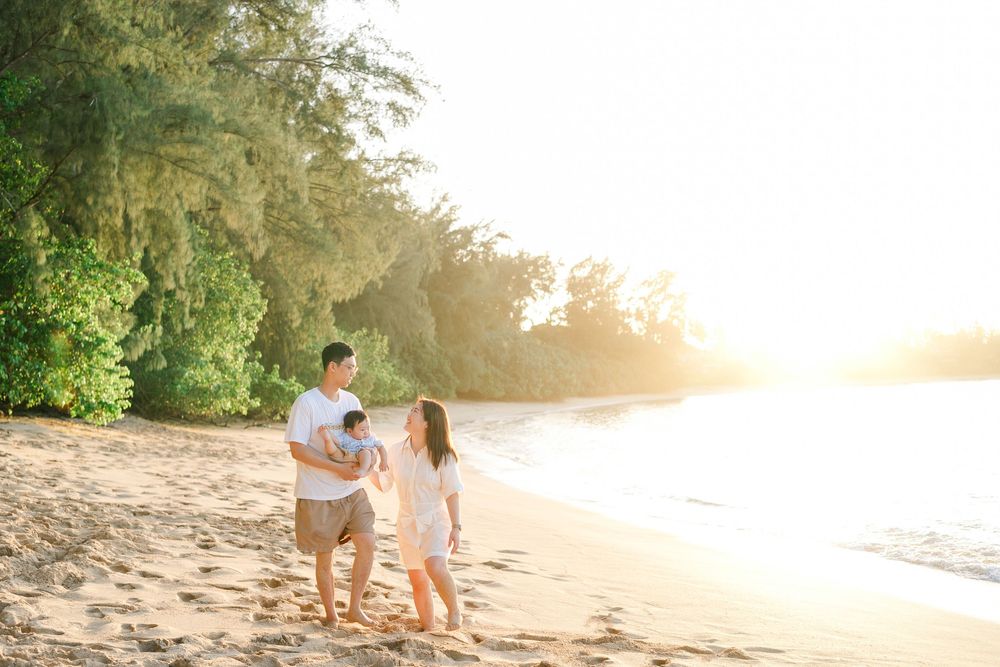 Couple walking on a sandy beach at sunset with golden sunlight filtering through trees.