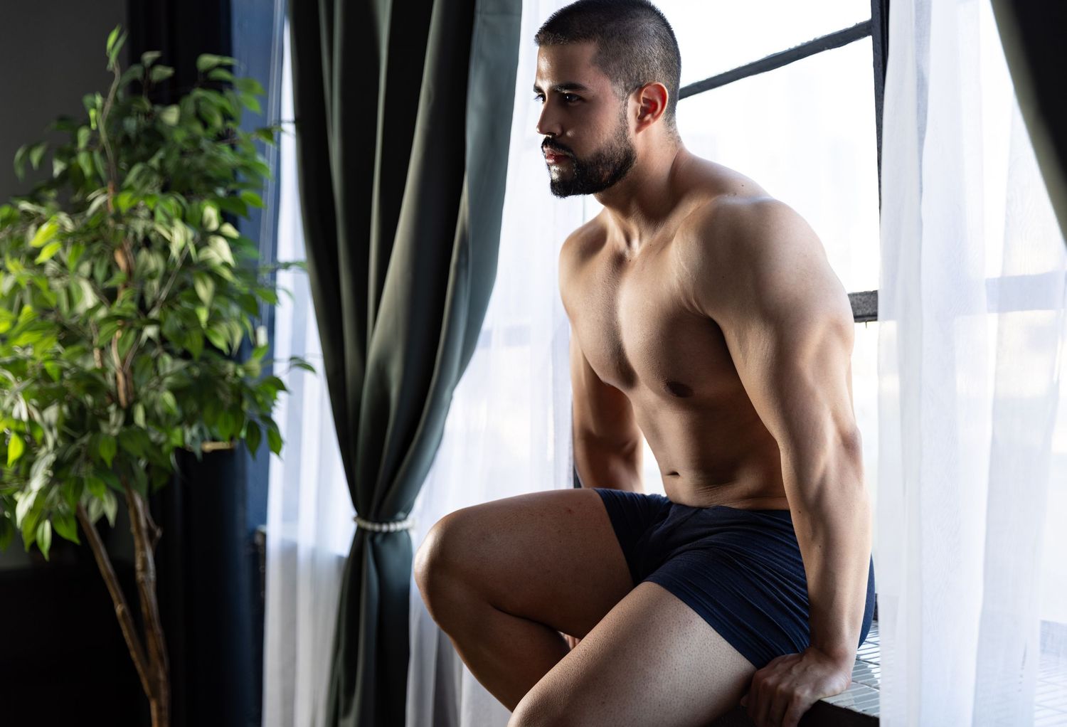 Photograph of man in underwear sitting on windowsill during boudoir photo session in Los Angeles.