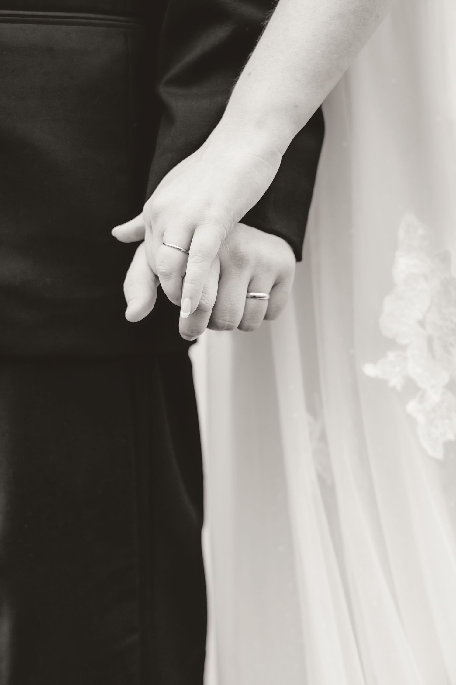 Black and white close-up of newlyweds holding hands showing wedding bands.