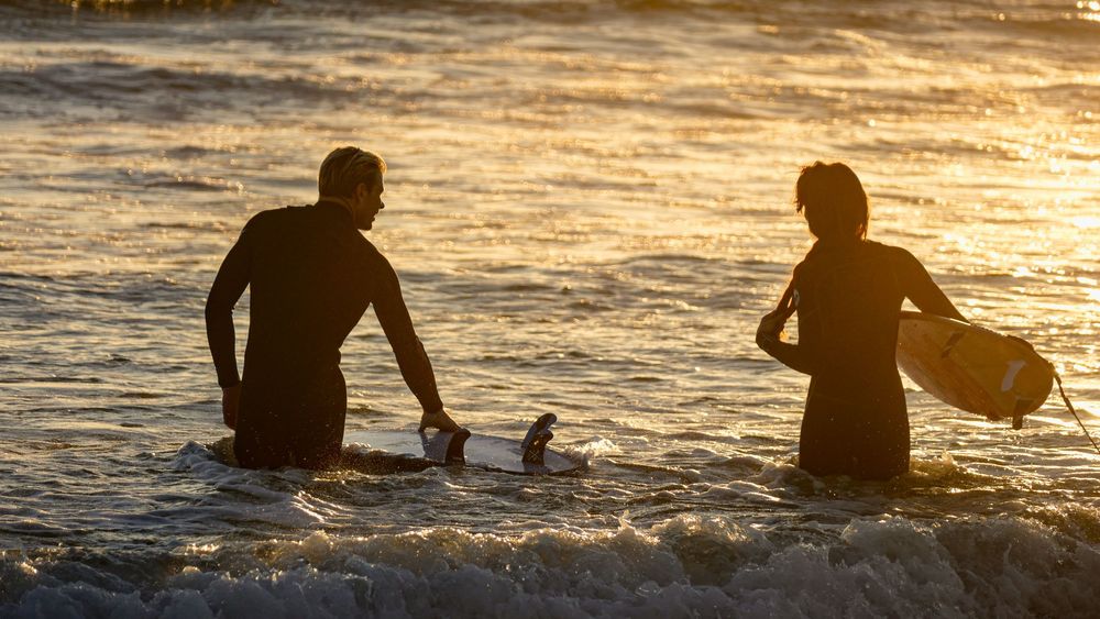 Silhouettes of people enjoying the water against a warm sunset backdrop at the beach.