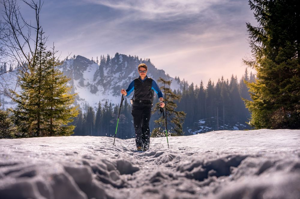 Cross country skier glides through snowy mountain landscape during winter sunset with dramatic cloudy sky.