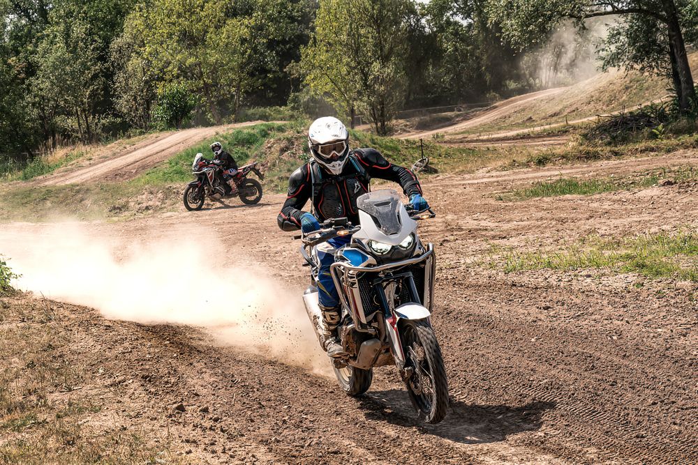 A sequence of dirt bike riders kicking up dust while racing through a winding off-road trail in a wooded area.