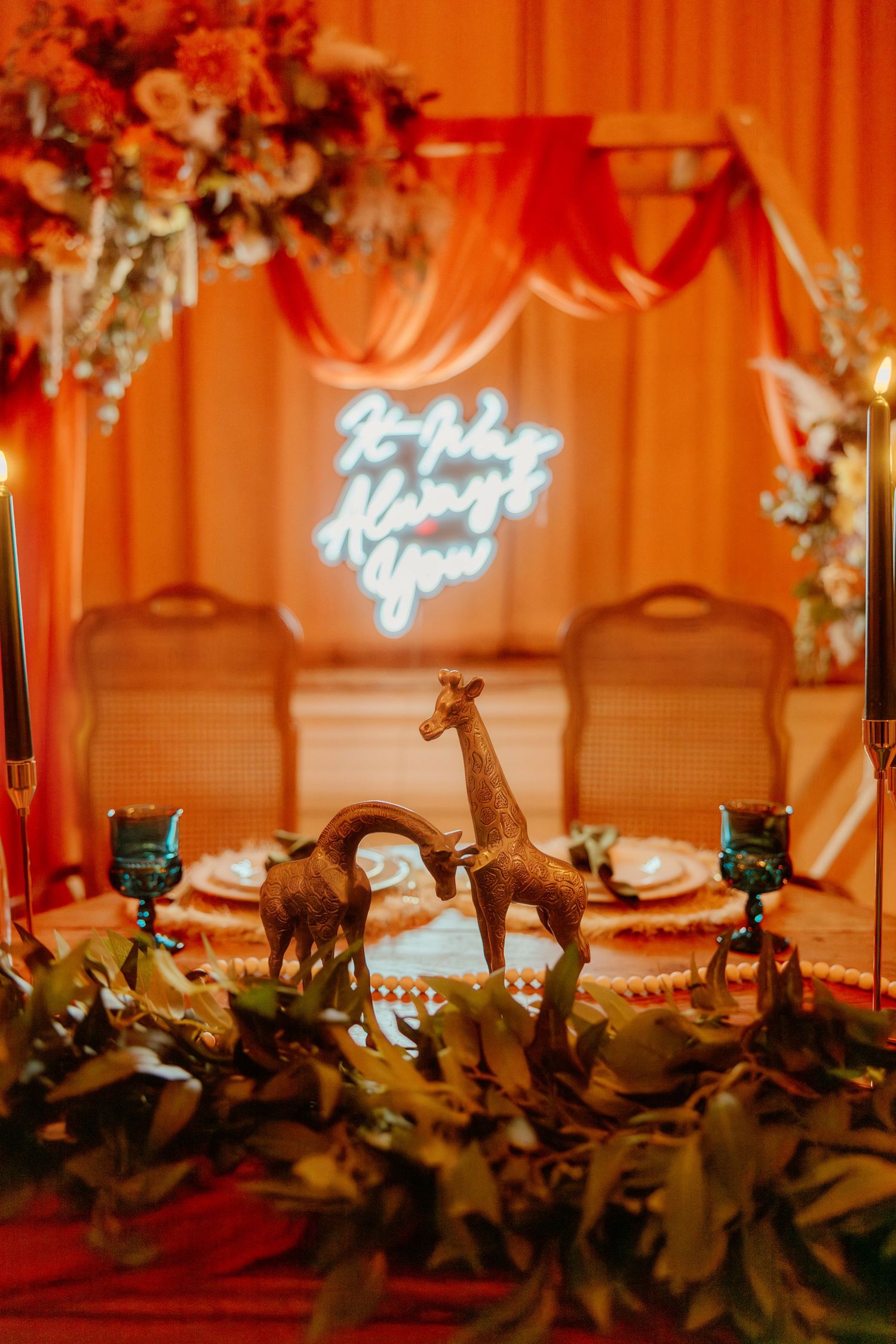 Wedding table decor with giraffe figurines and neon sign against orange draped backdrop.