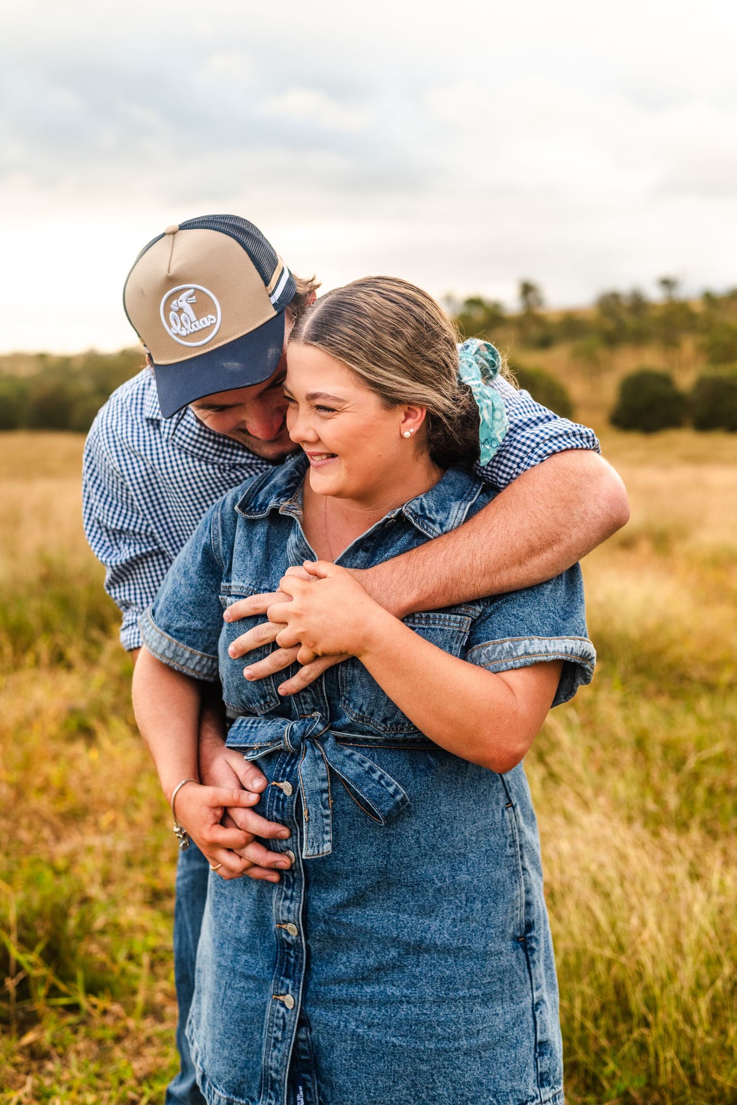 A couple in denim sharing an intimate embrace in a sunlit field.