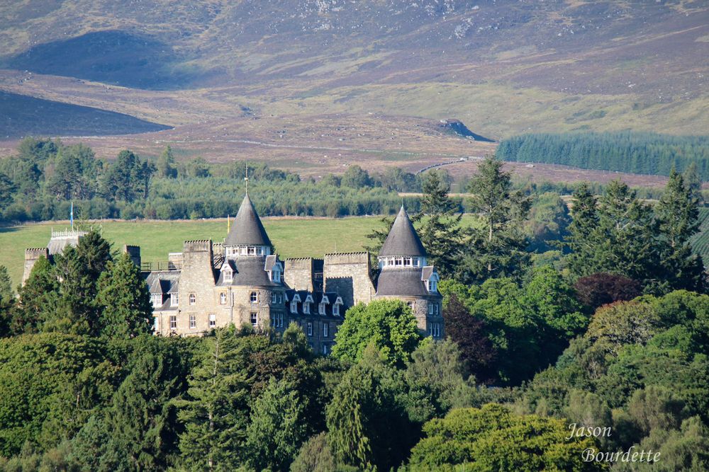 Atholl Palace in Scotland viewed from a distance, nestled among rolling hills and surrounded by lush greenery