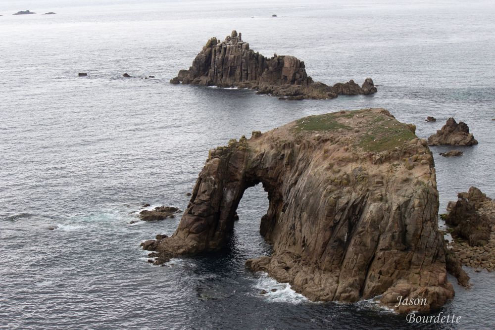 Enys Dodnan Arch, a stunning natural rock formation off the coast of Cornwall, standing gracefully against the backdrop of the deep blue sea