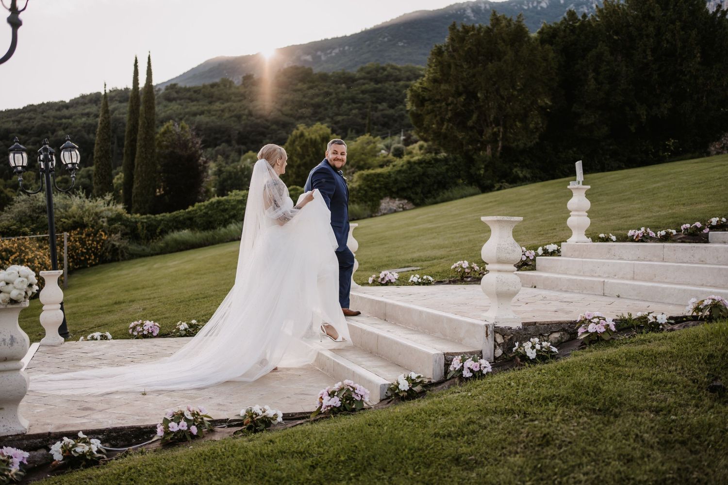 Newlyweds stand on white steps against a mountain backdrop in an outdoor wedding setting.