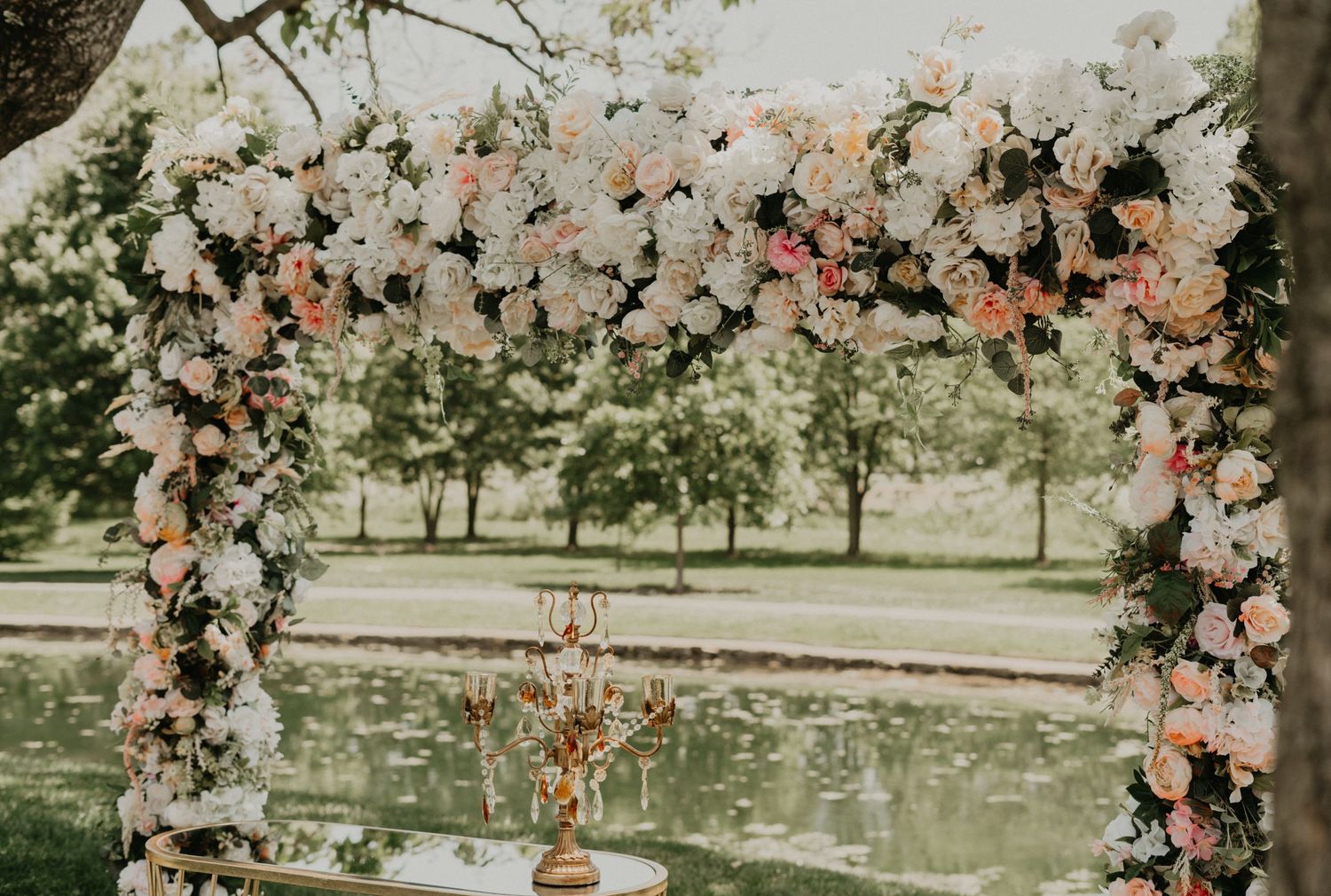 Wedding arch decorated with pink and white flowers in a garden setting.